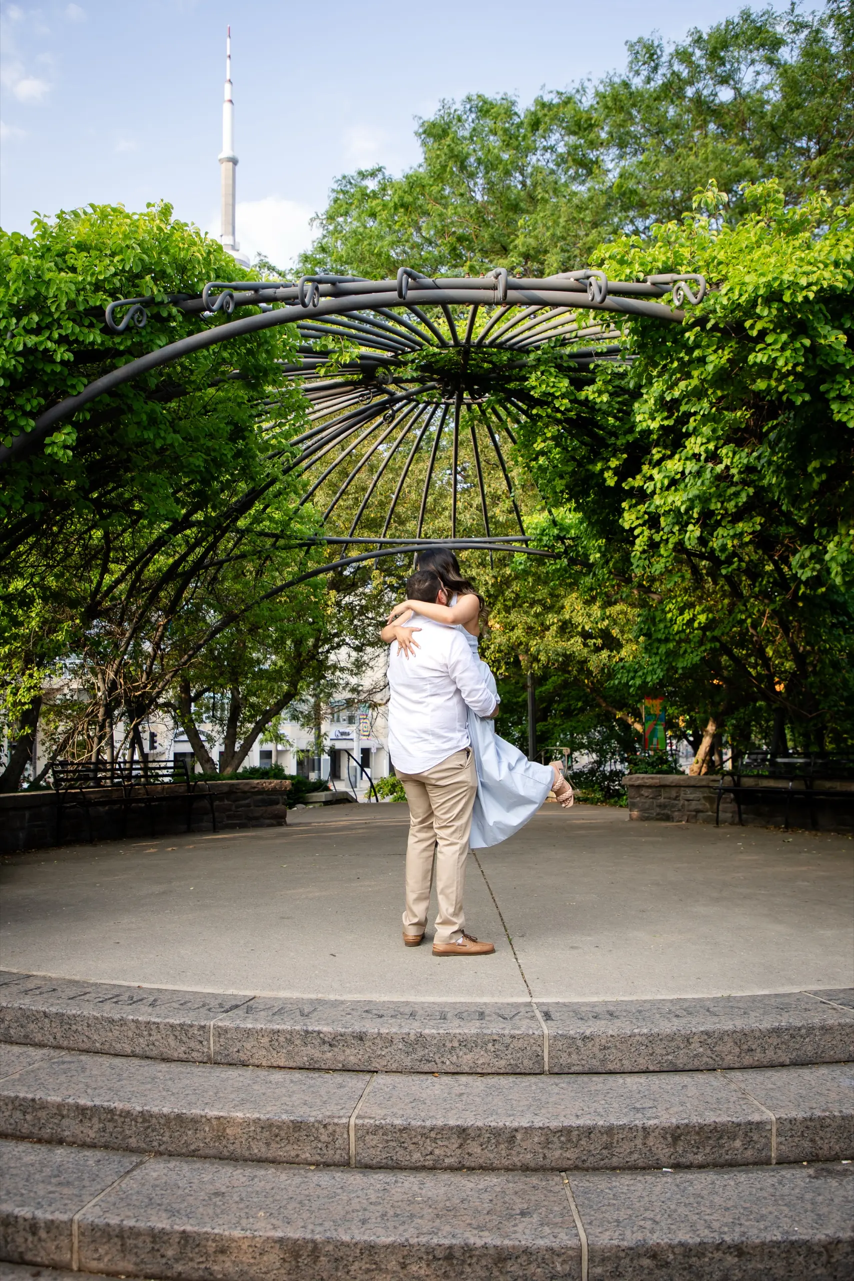 Mike lifting Margarita off the ground at the Toronto Music Garden with the CN Tower in the background, by AD Photography