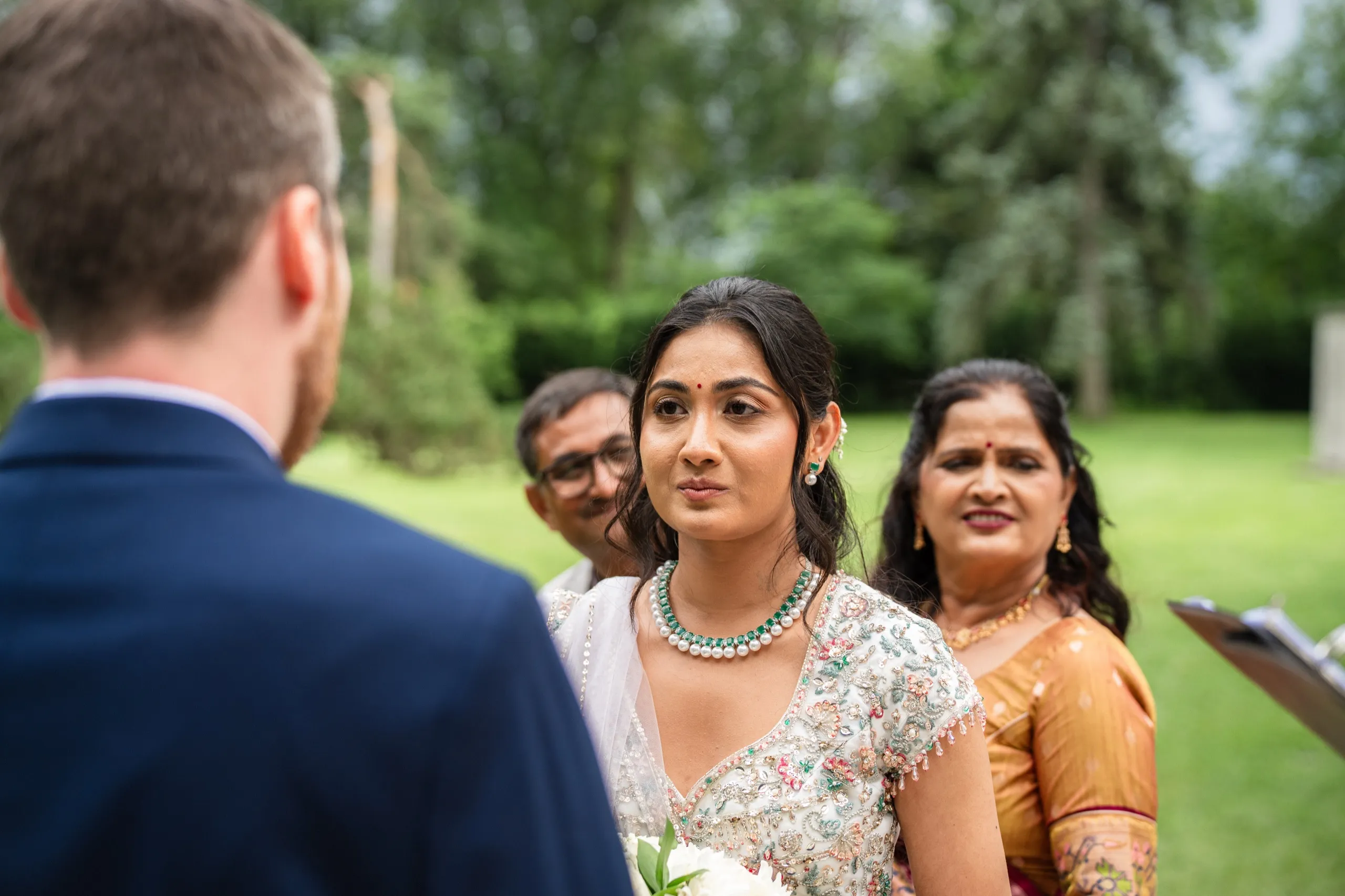 Nidhi looks past Derek's shoulder toward her parents, emotion plain on every face., by AD Photography