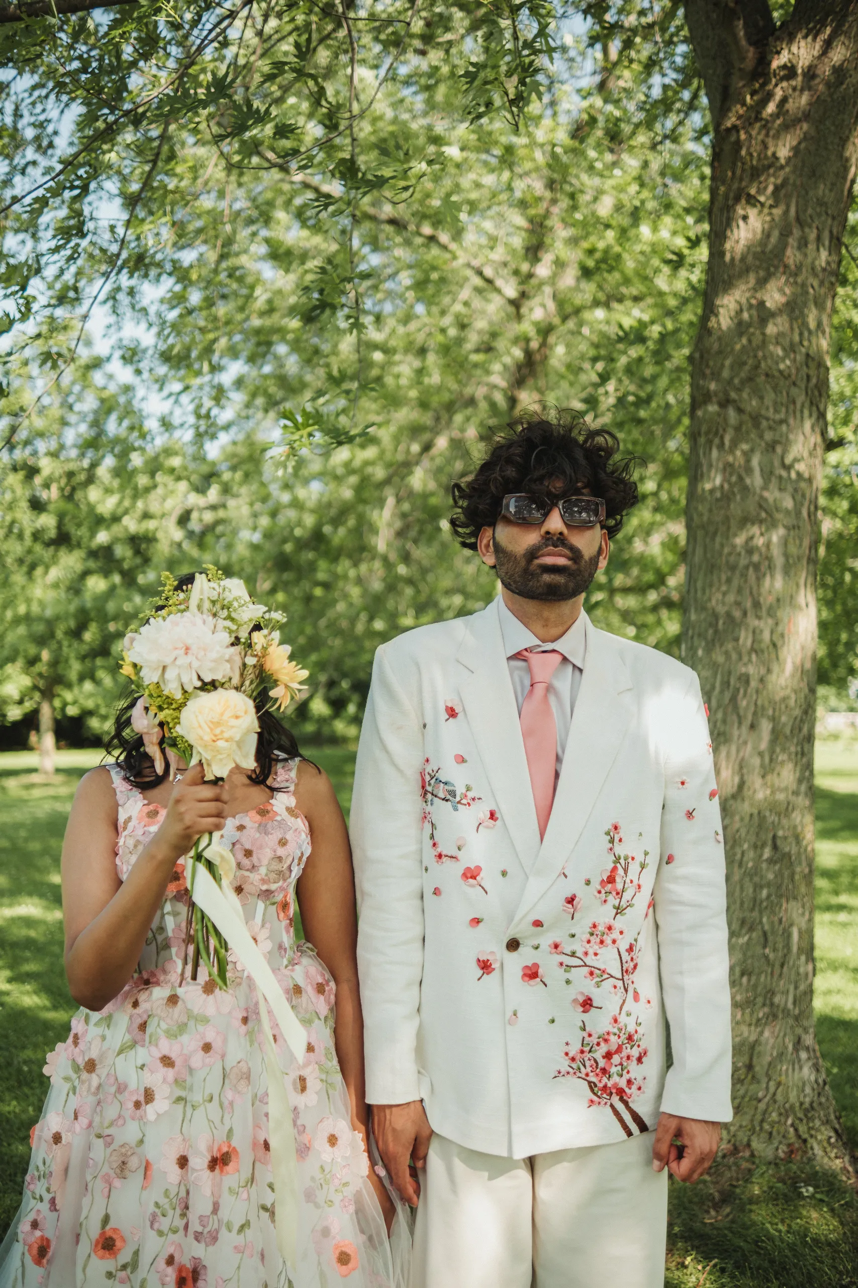 Payal hiding her face behind her bouquet beside a deadpan Harsh in sunglasses, Toronto Islands, by AD Photography