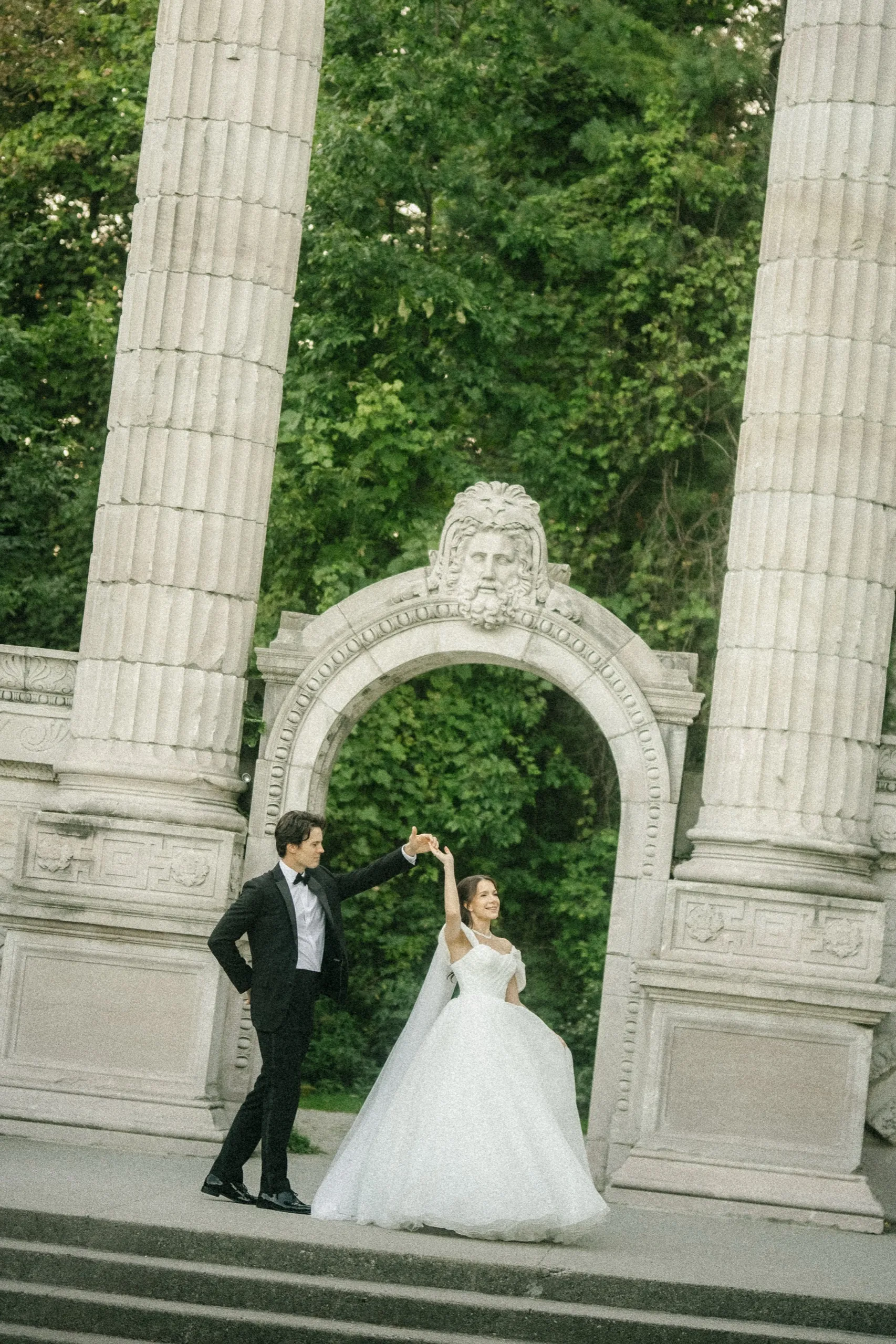 Couple twirling inside a carved stone archway between two fluted columns, by AD Photography
