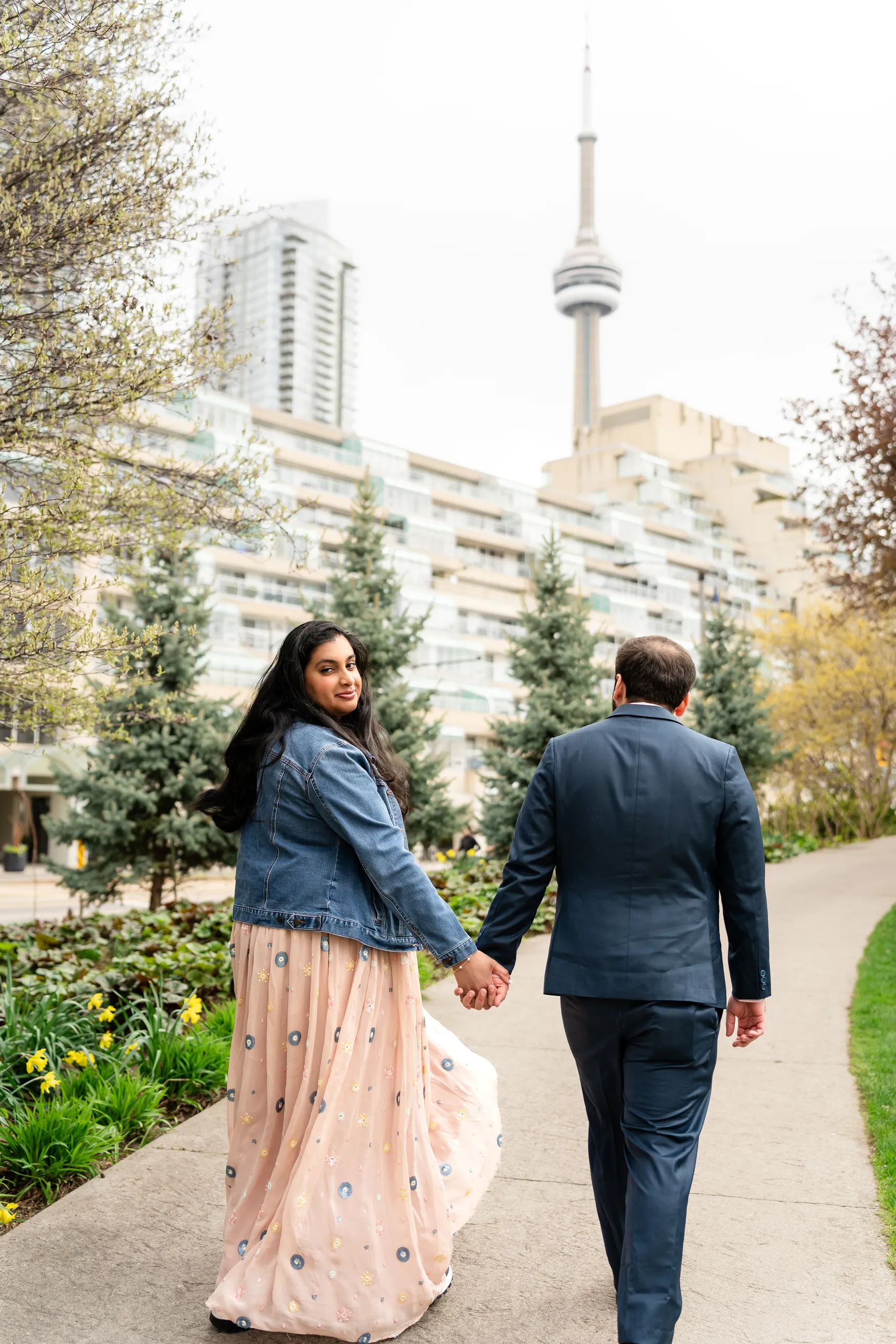 Nadia looks back over her shoulder as the couple walk hand in hand toward the CN Tower, by AD Photography