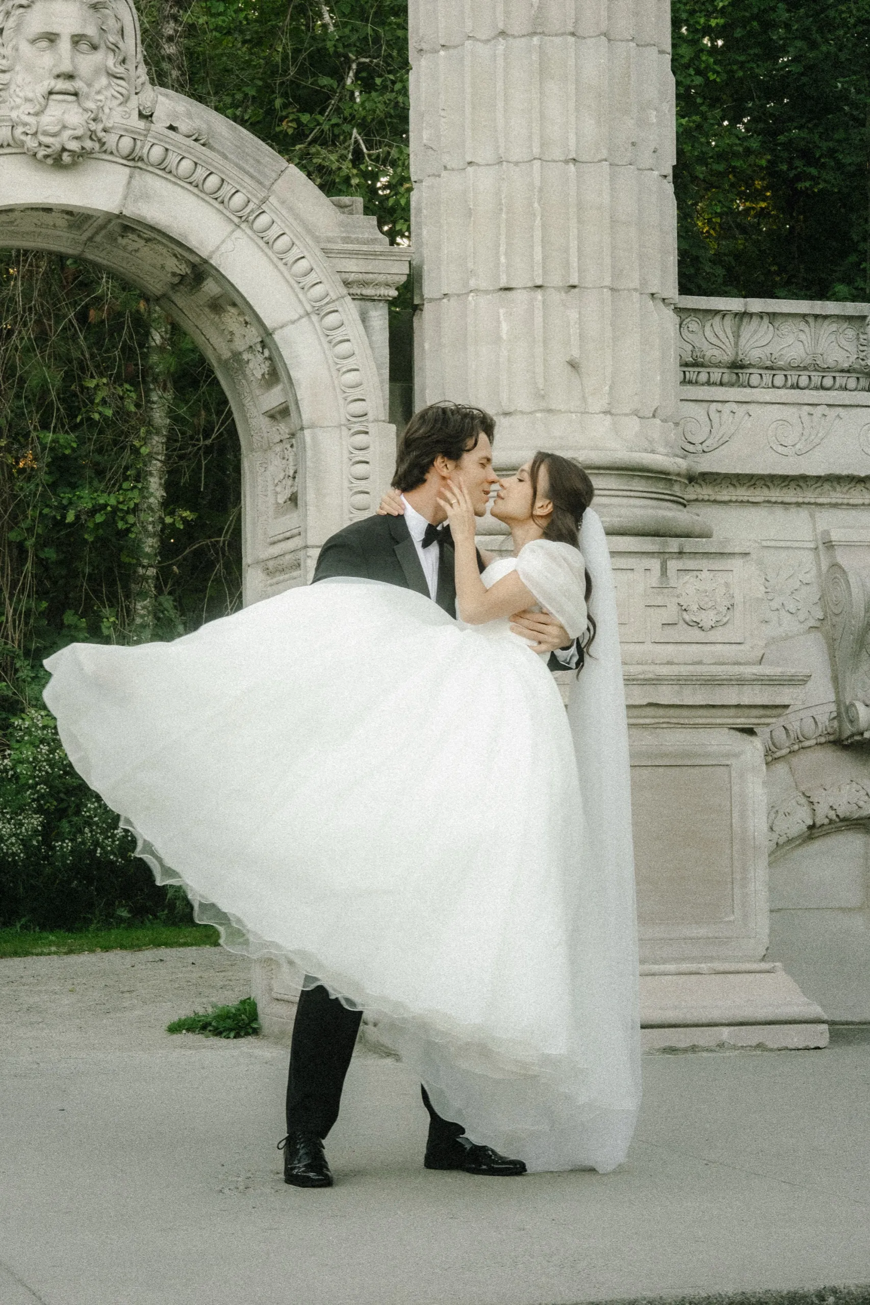 Groom lifting the bride beneath the carved arch as her tulle skirt fans out, by AD Photography