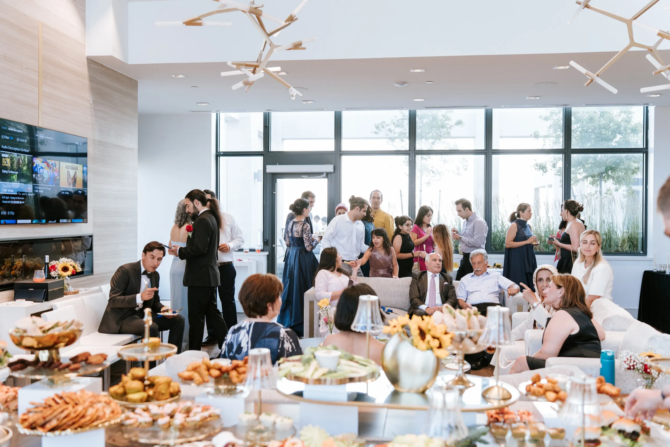 Guests fill the couches while the grazing table stretches across the Maple party room at the height of the celebration, by AD Photography
