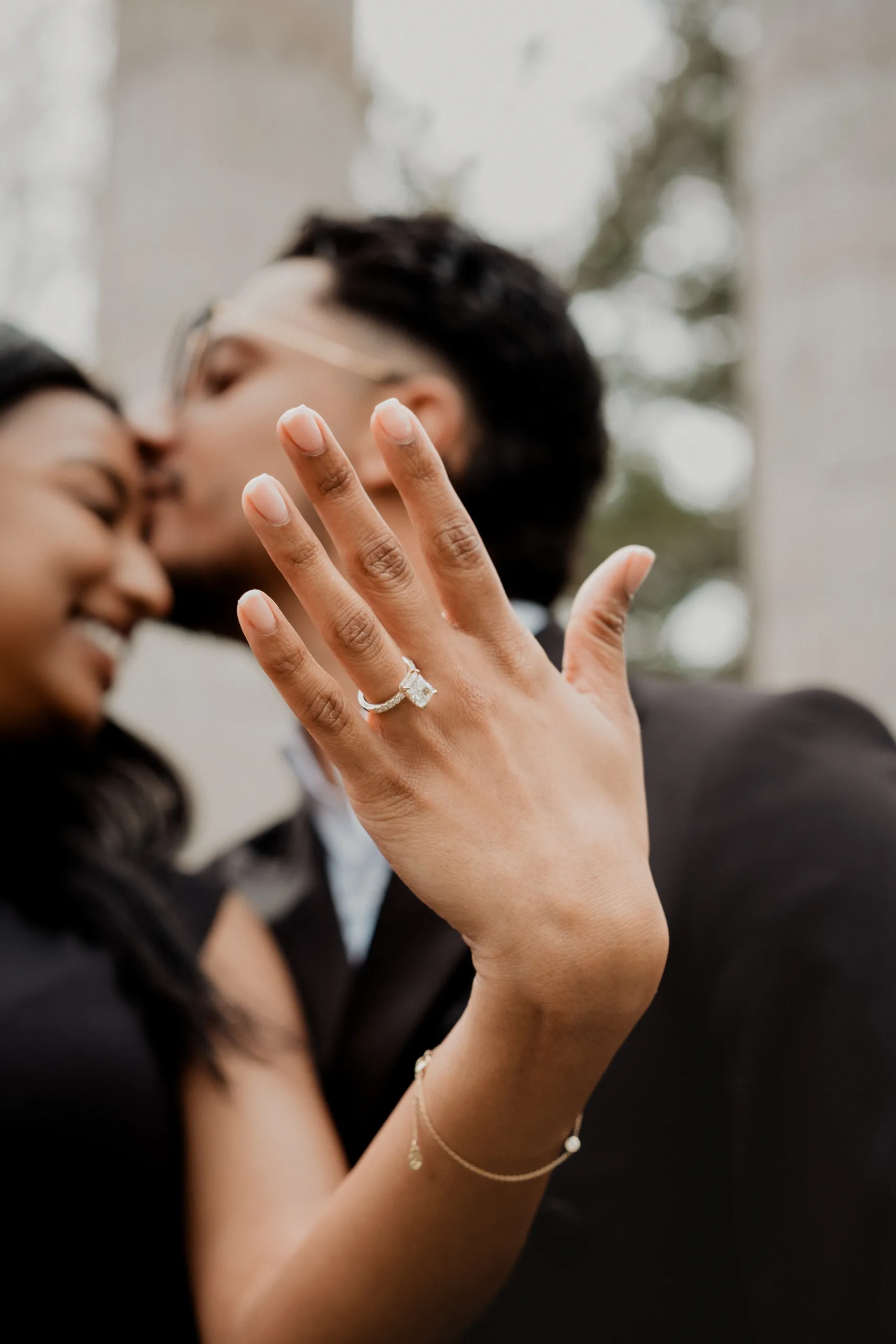 Lavina's hand raised to the camera, ring sharp, Raeed kissing her temple just behind it, by AD Photography
