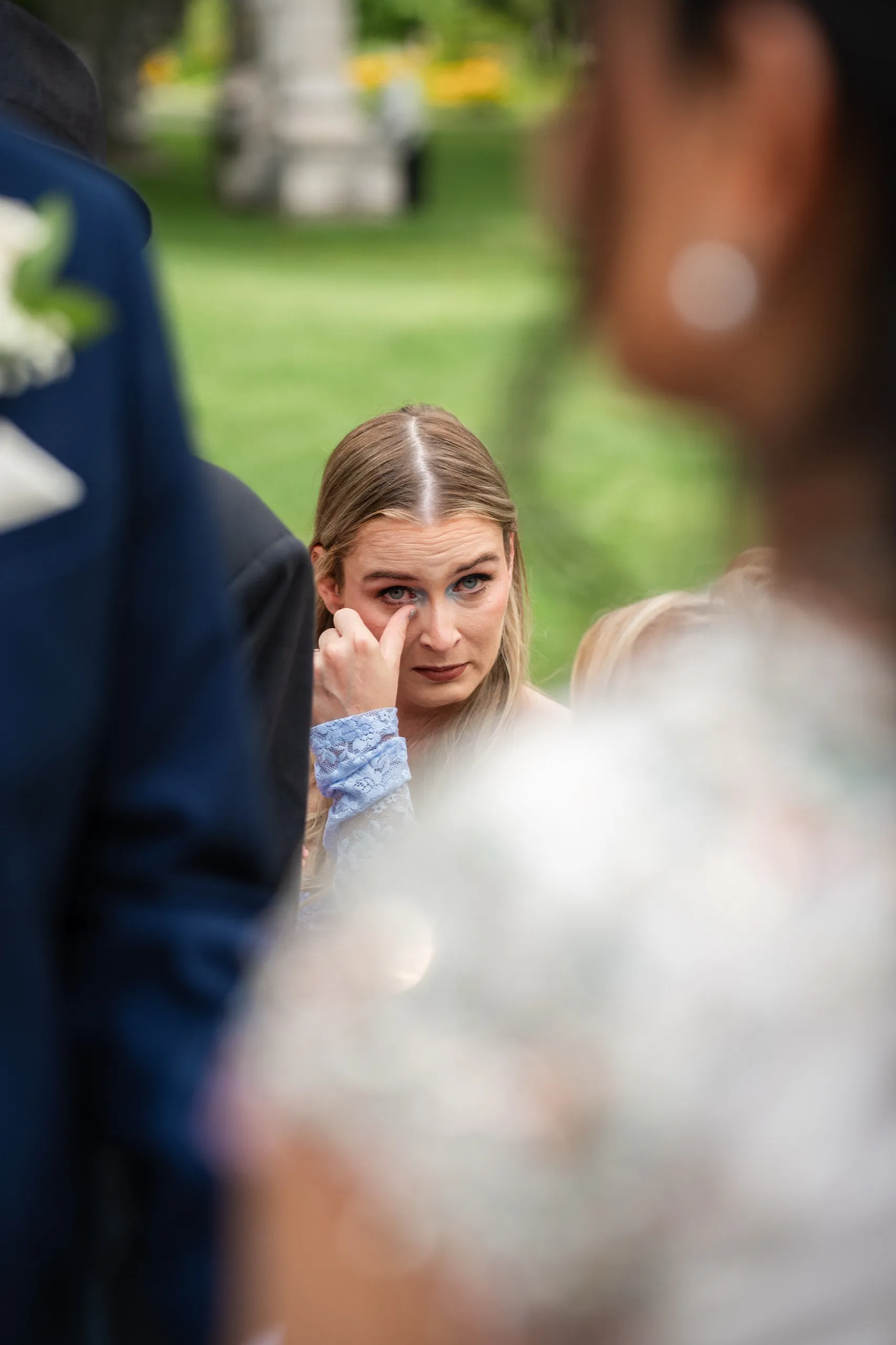A guest wipes away a tear during the civil ceremony, framed through soft foreground blur., by AD Photography