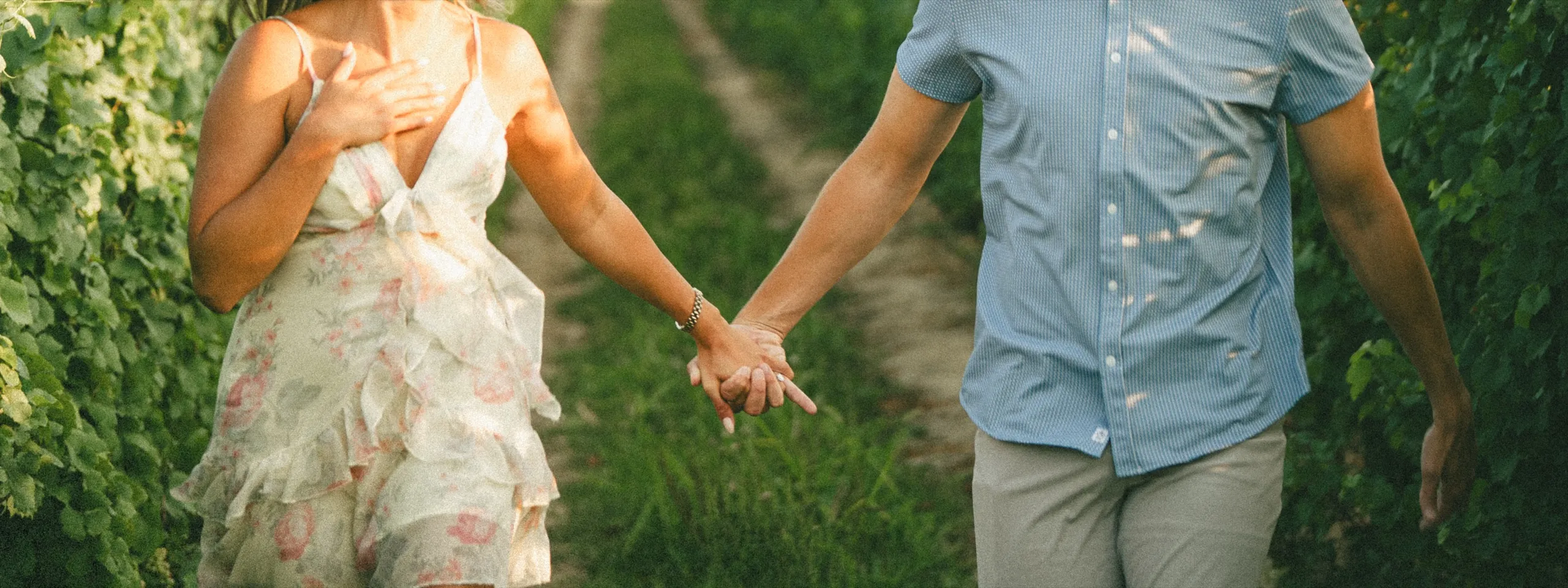 Linked fingers between them as they walk a grass row through the vineyard, faces out of frame, by AD Photography