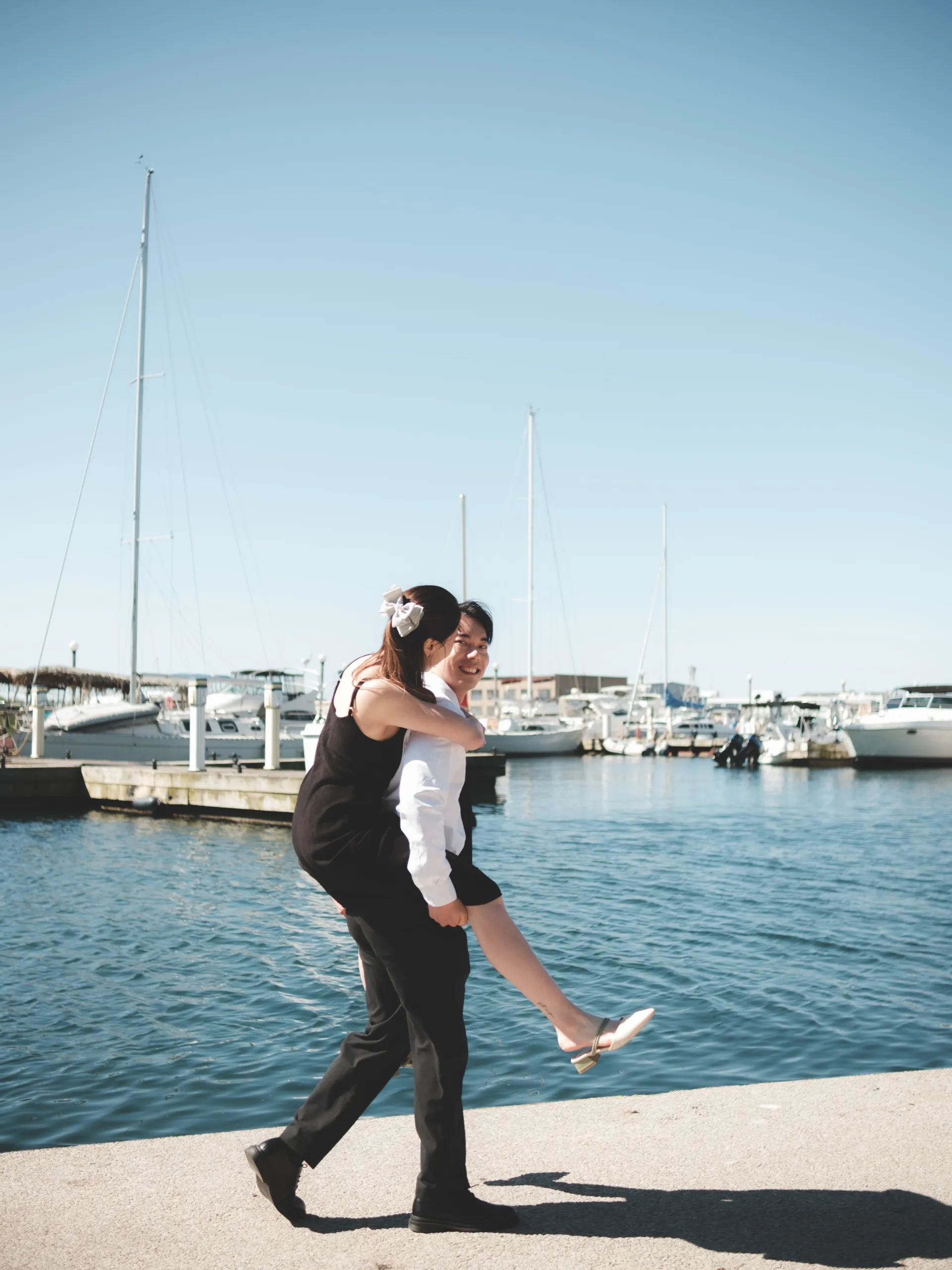 Josie playfully lifts Nelson off the ground at the marina with sailboats behind, by AD Photography