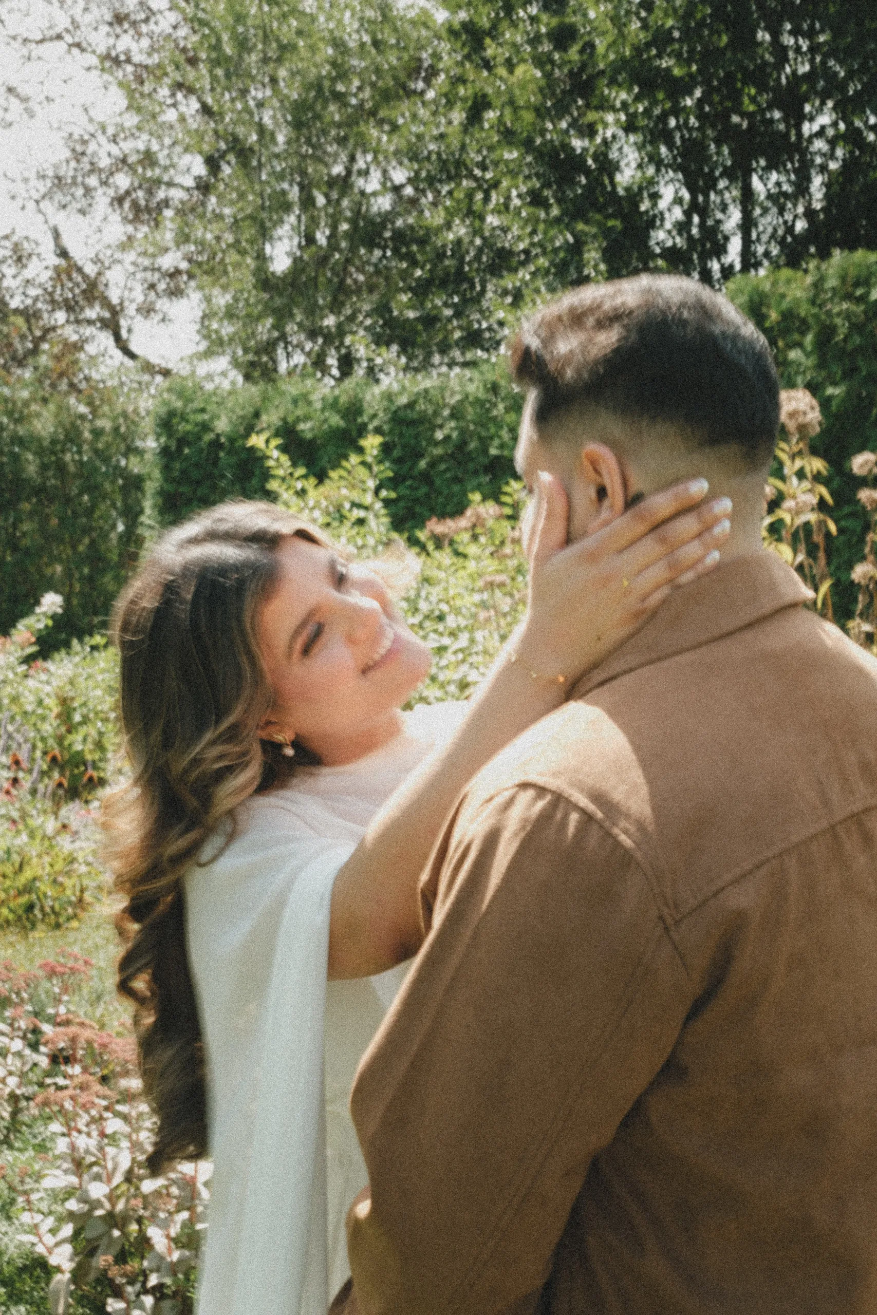 Seen over Maninder's shoulder, Parneet laughs with her hand on his cheek in a late summer garden, by AD Photography