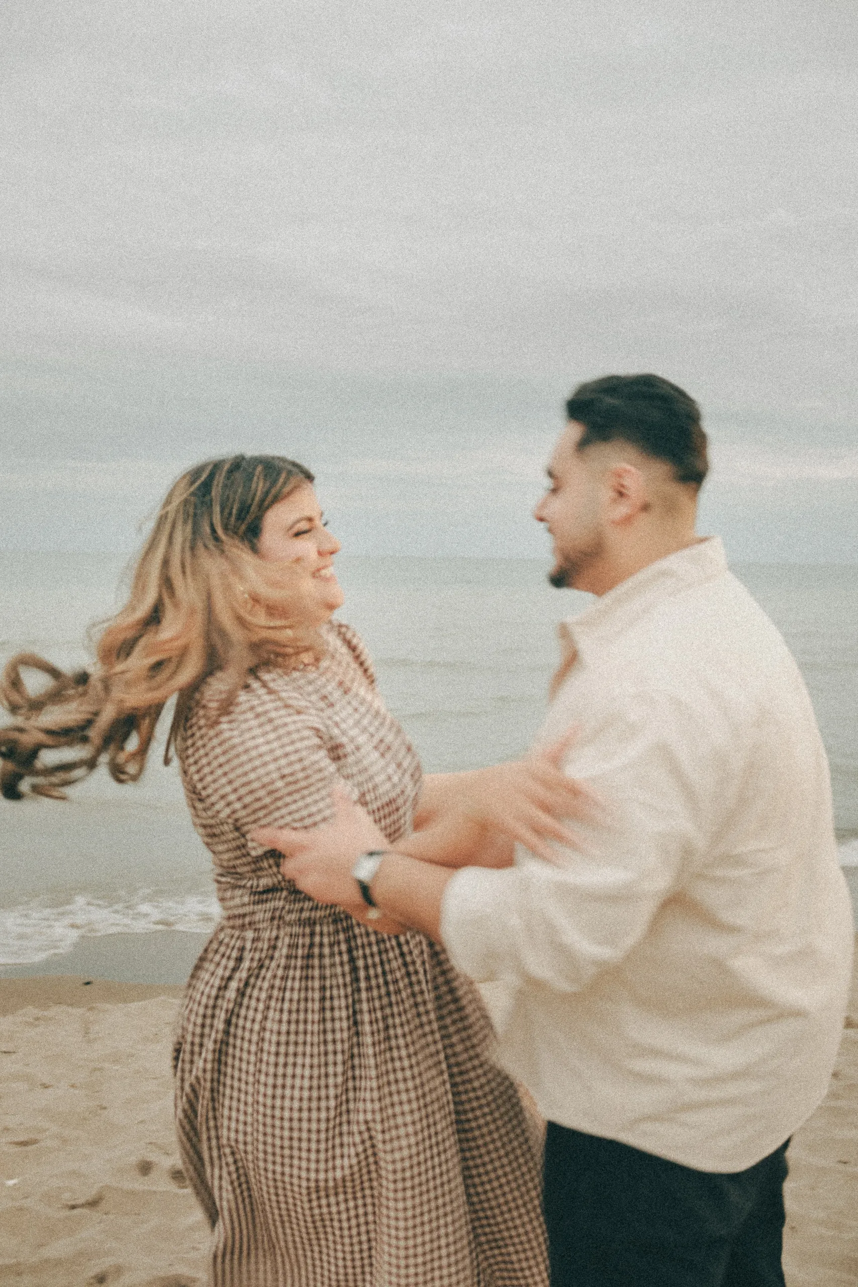 Motion blur of Parneet spinning into Maninder's arms, hair whipping, under grey evening cloud by Lake Ontario, by AD Photography