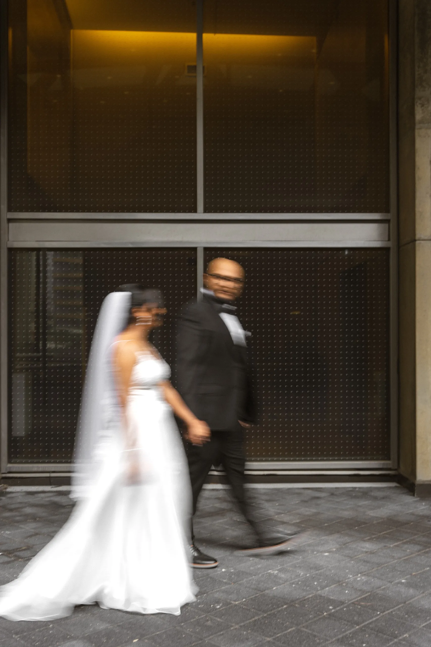 Motion blur of the newlyweds walking past the City Hall concrete columns, by AD Photography