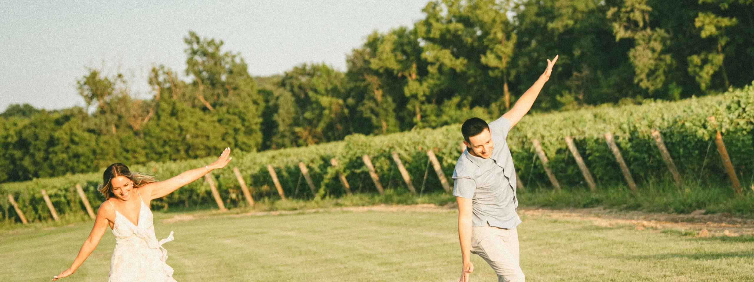 The two of them mirrored with arms flung wide on the mown lawn above the vines, by AD Photography