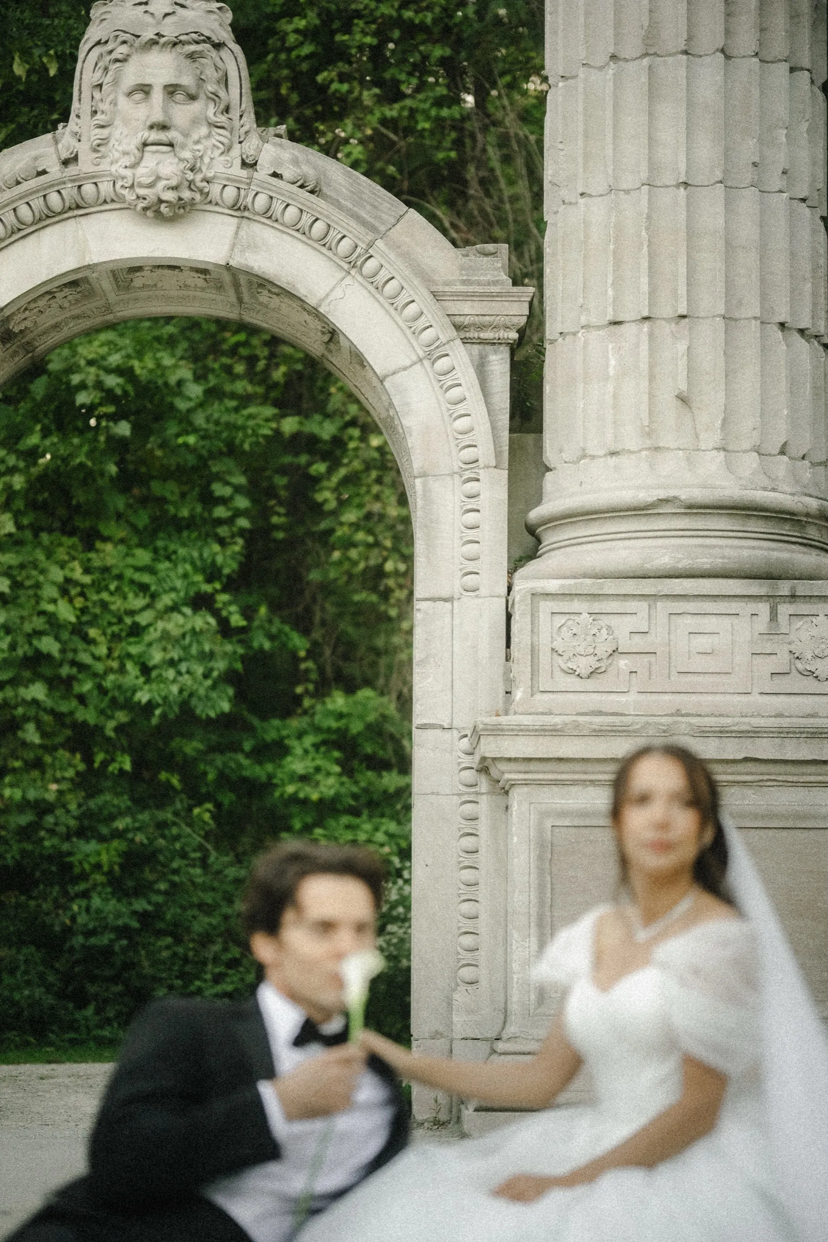 Carved archway and column in sharp focus while the bride and groom sit soft below with a calla lily, by AD Photography