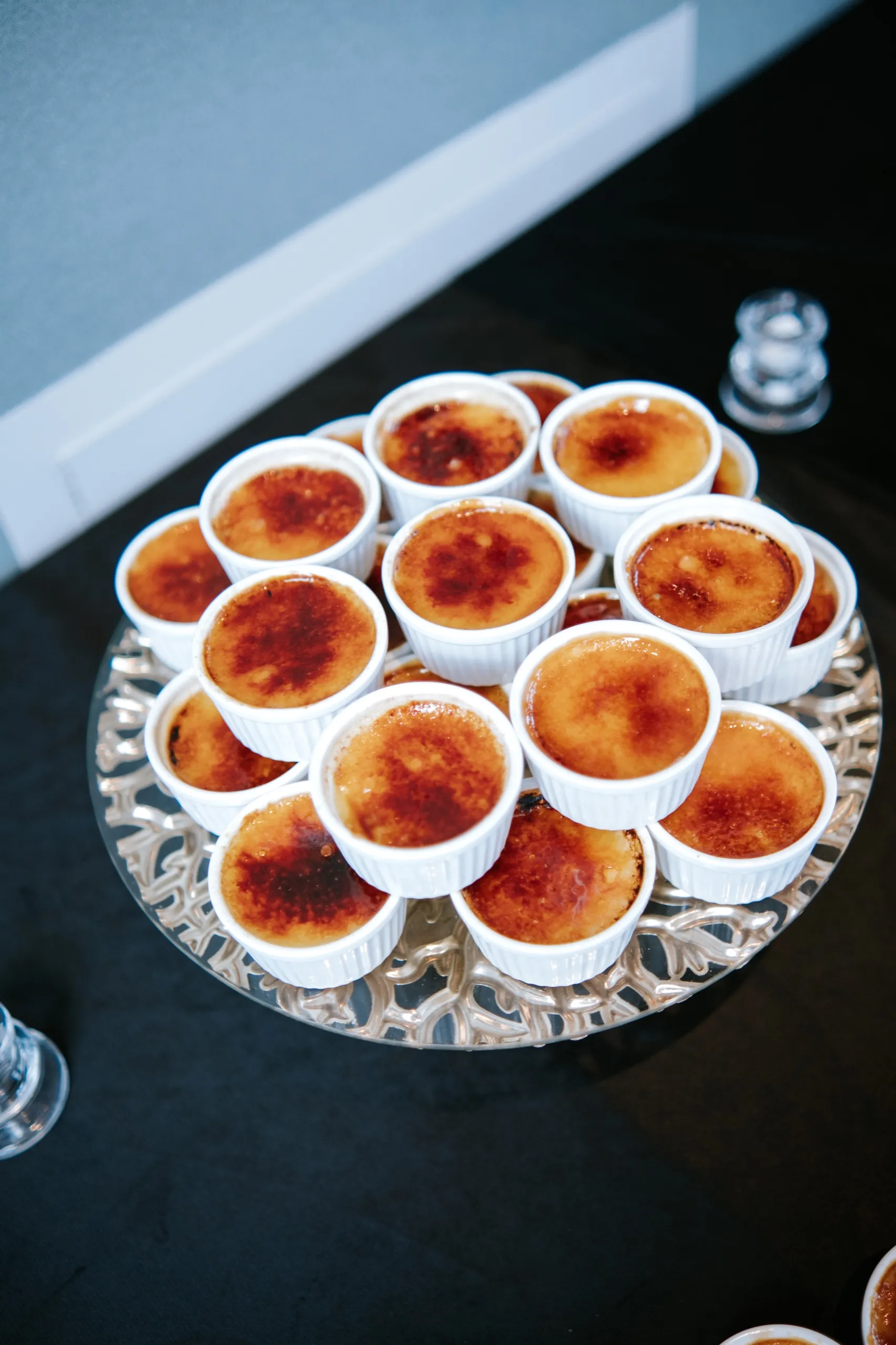 A silver stand of creme brulee cups waiting on the black dessert table, by AD Photography