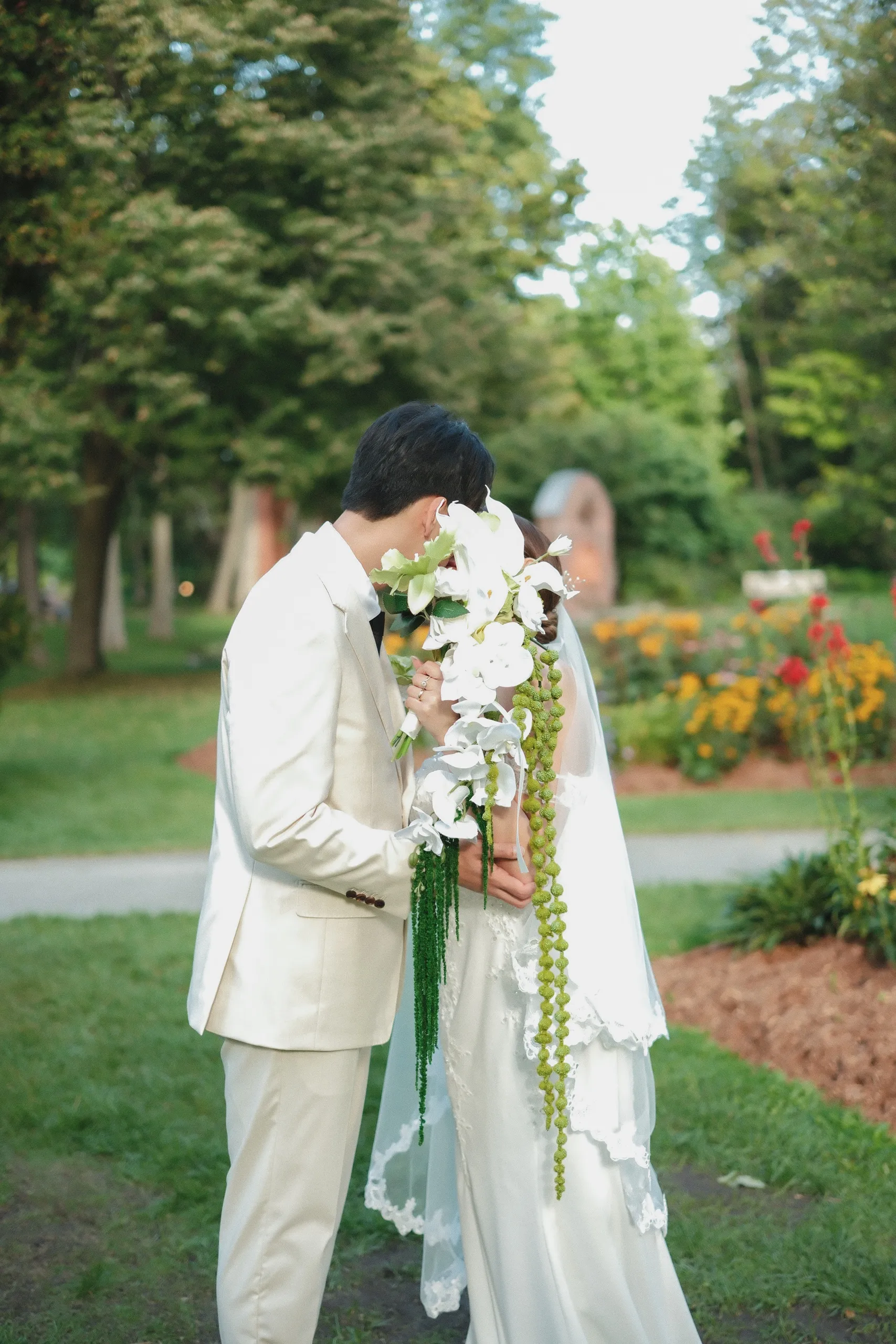 Nelson leaning in to kiss Josie behind her cascading orchid bouquet, by AD Photography