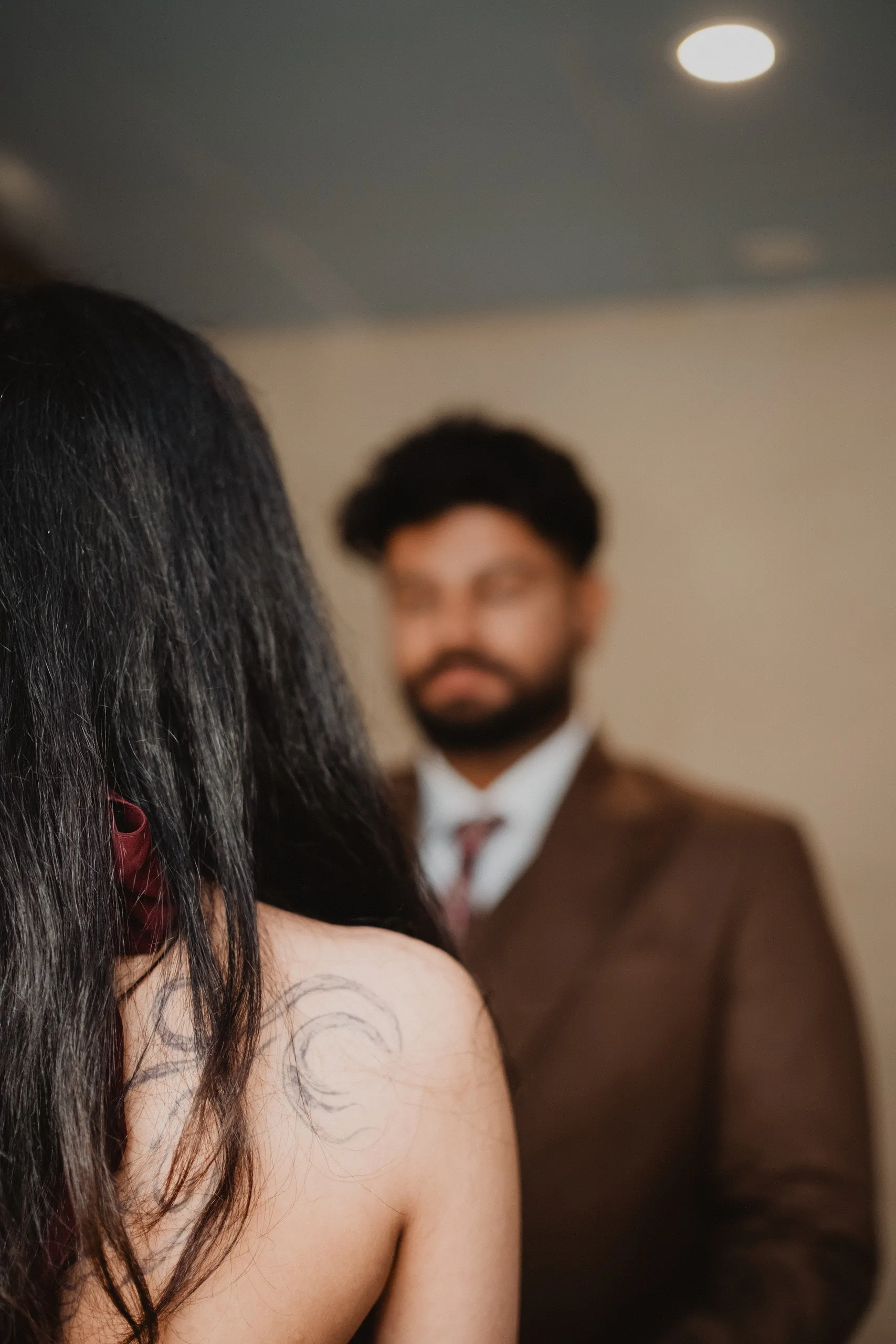 Soft focus frame of the bride's shoulder tattoo with Kamal blurred just behind her, by AD Photography
