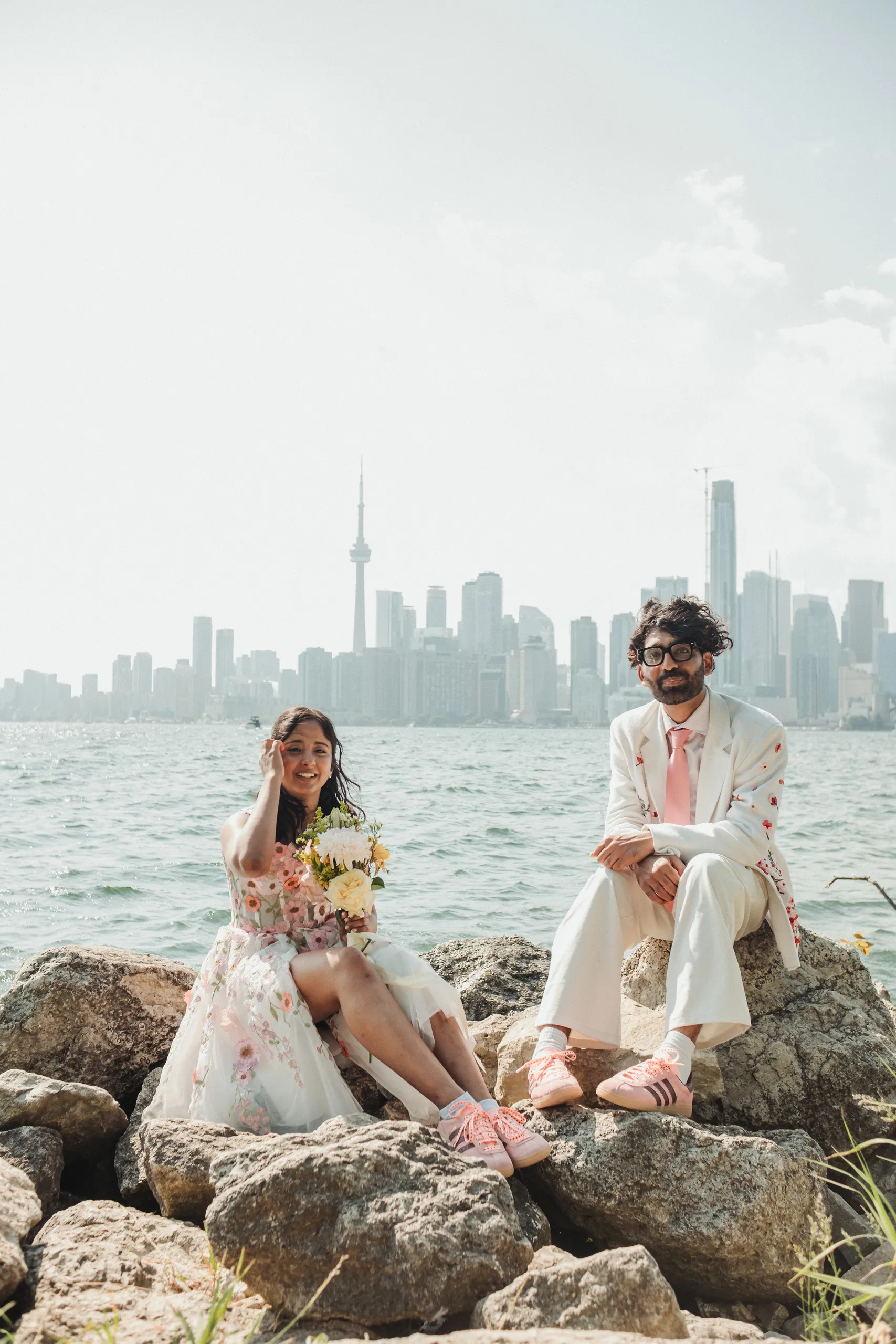 Harsh and Payal laughing together on the rocks with the Toronto skyline behind them, by AD Photography