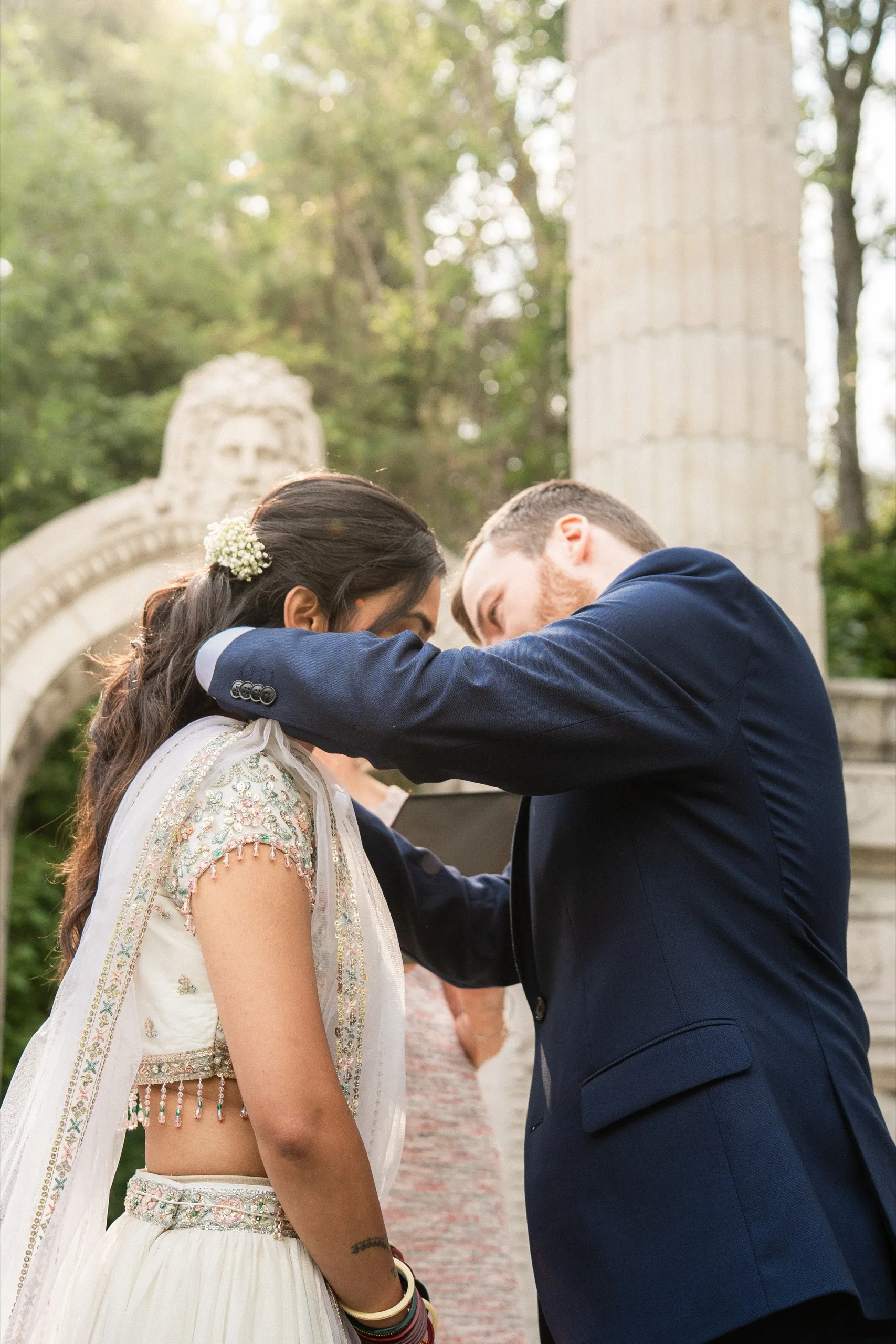 Derek fastens Nidhi's dupatta at her shoulder as the officiant waits beside the arch., by AD Photography