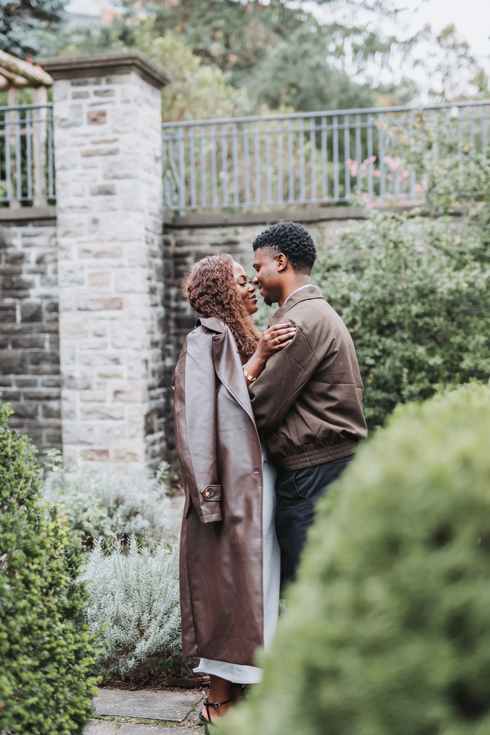 Richie and Aimee nose to nose in a hedged garden corner, seen past a soft clipped hedge, by AD Photography