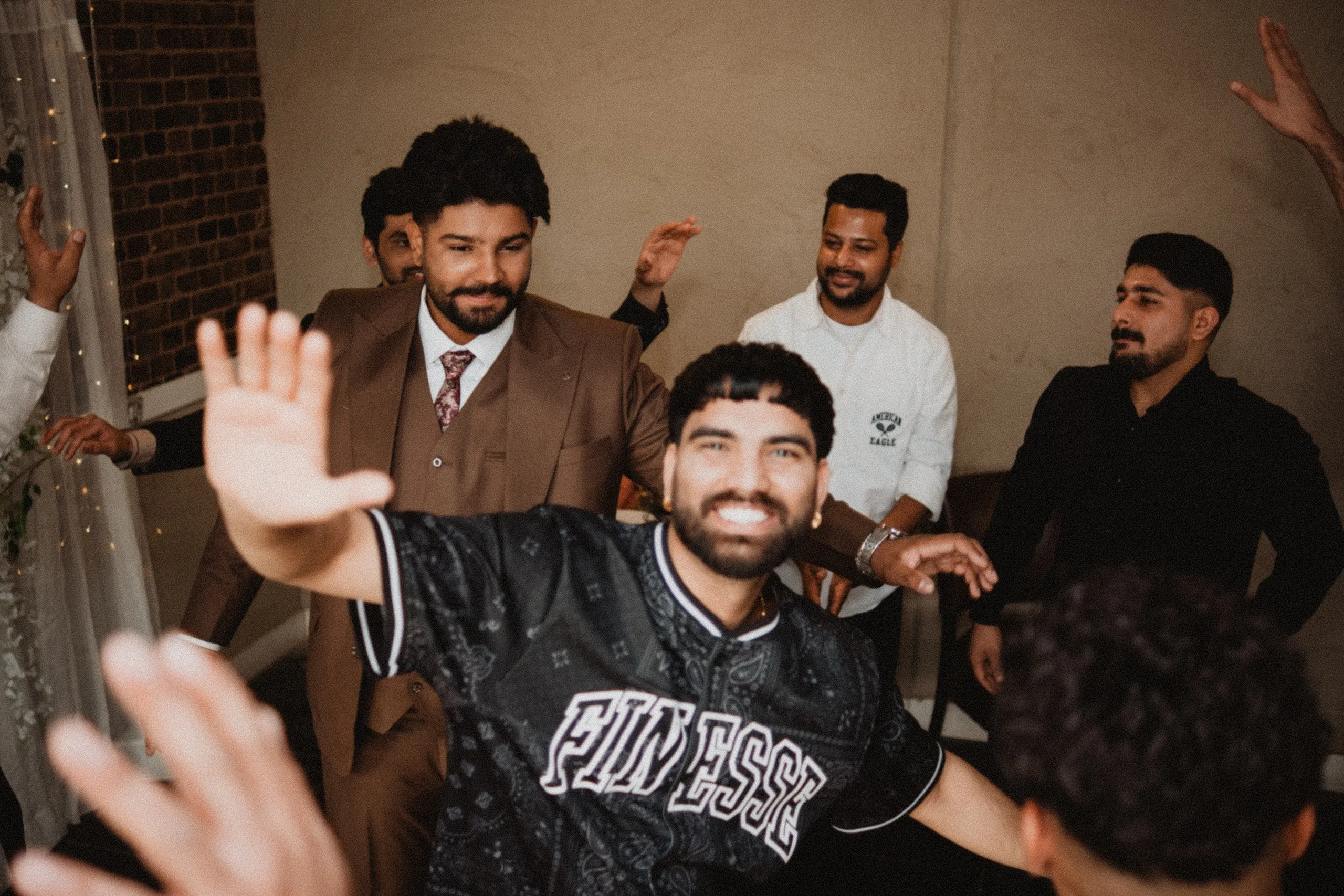 Friends throwing their hands up around Kamal on the reception dance floor, by AD Photography