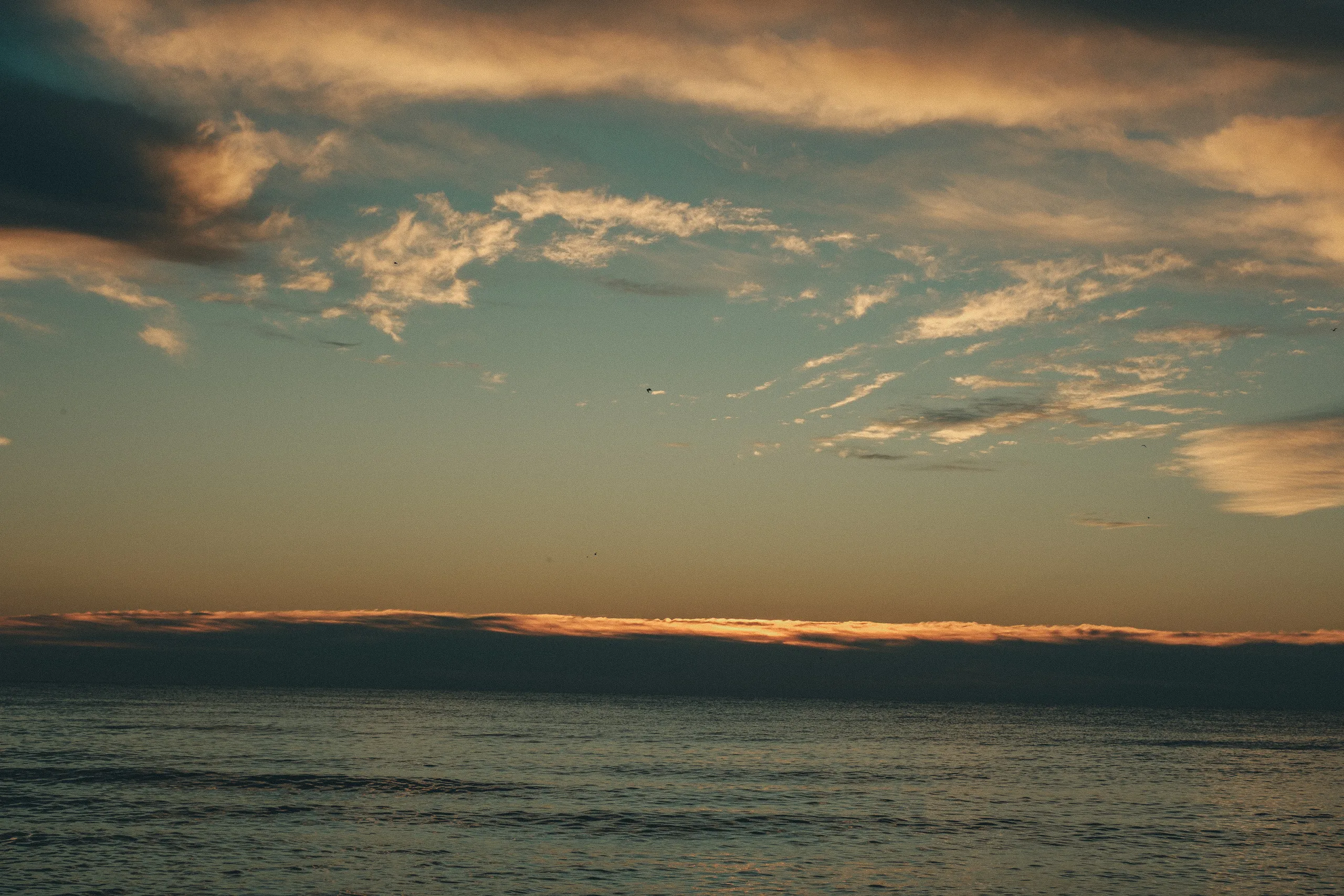 Grainy first light over Lake Ontario, the sun still behind a low glowing bank of cloud, by AD Photography