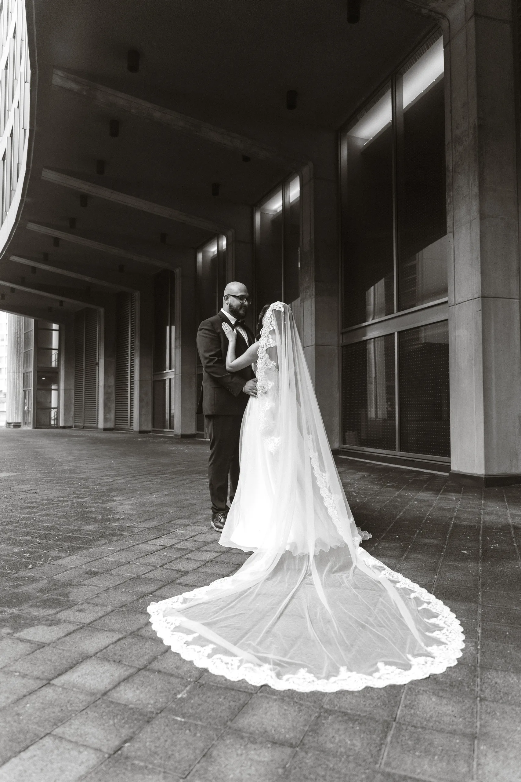 Black and white portrait of the couple with the cathedral veil spread across the pavement, by AD Photography