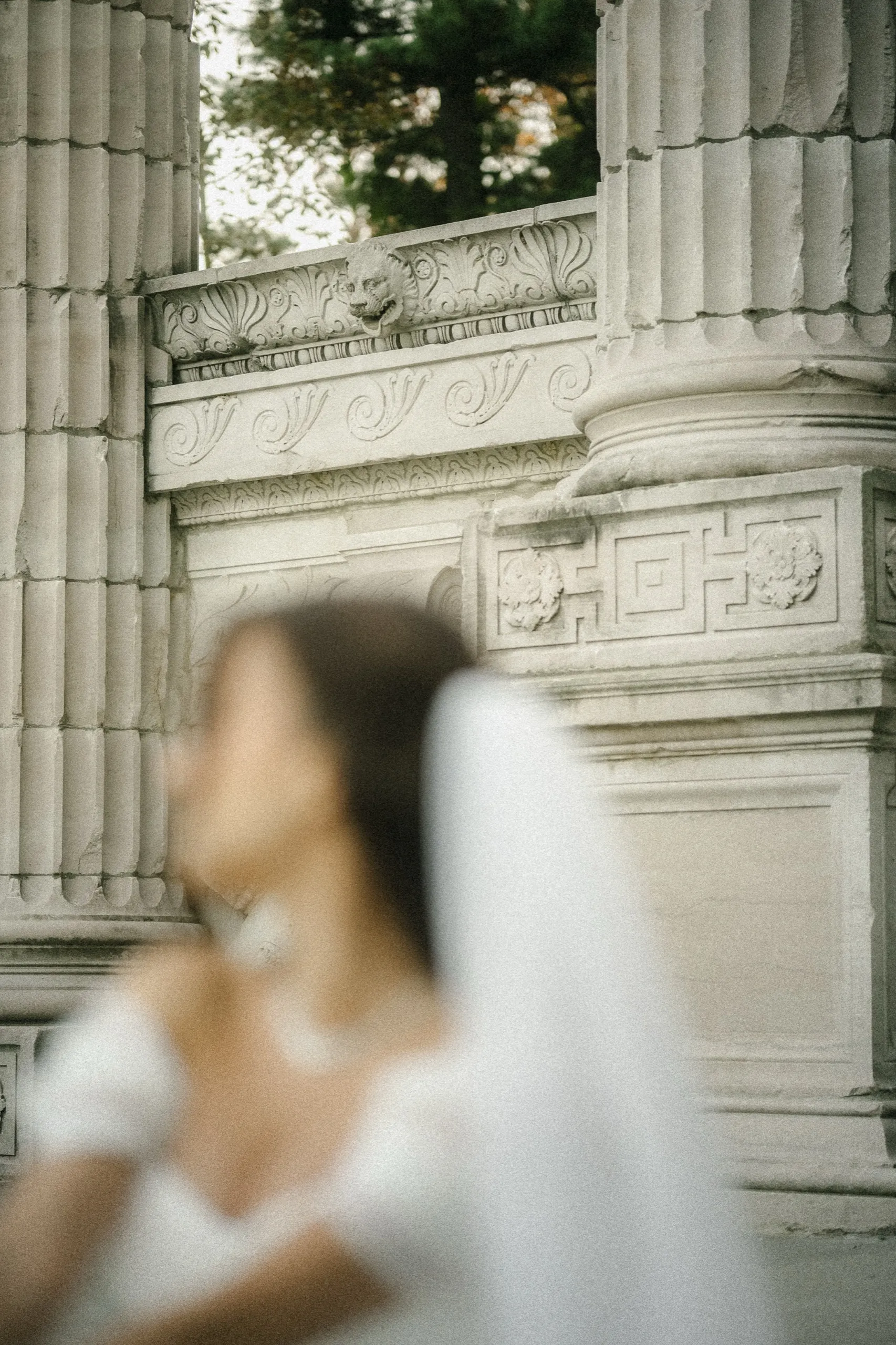 Carved stone frieze and fluted column in focus as the veiled bride turns away, soft in the foreground, by AD Photography