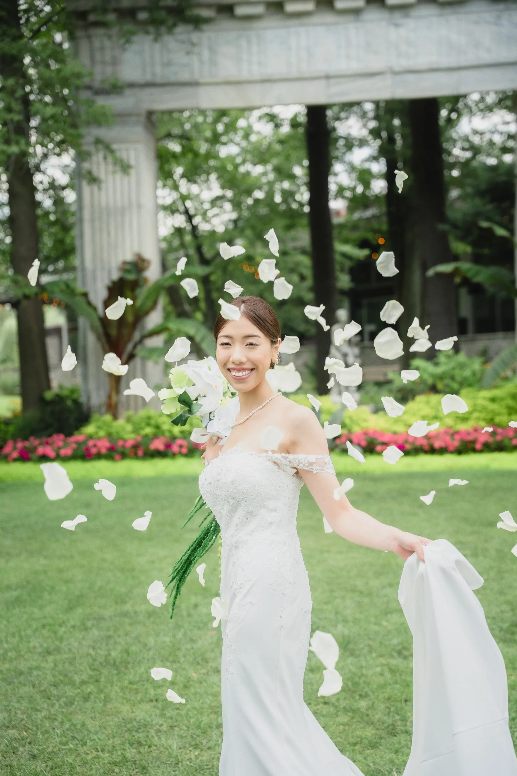 Josie laughing in a shower of white rose petals, gown train in hand, by AD Photography