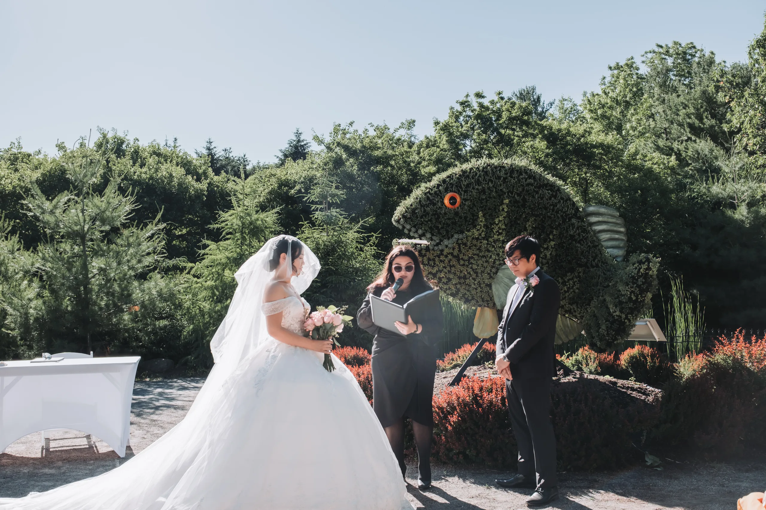 The officiant reading beside the giant green fish topiary as Karen and Micheal marry in Niagara Falls, by AD Photography
