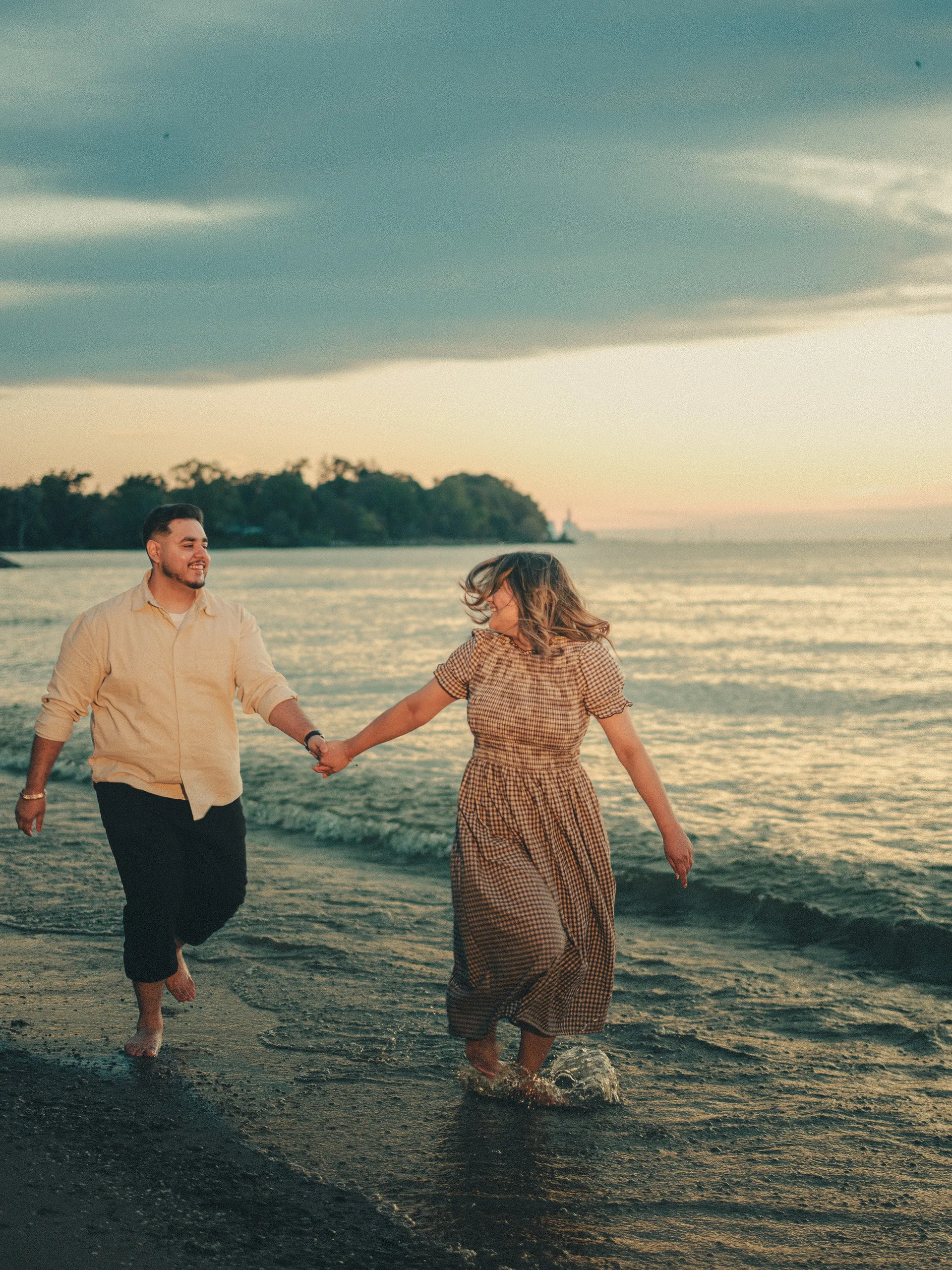 Barefoot and hand in hand at sunrise, Parneet kicks a splash in the shallows as Maninder laughs, by AD Photography