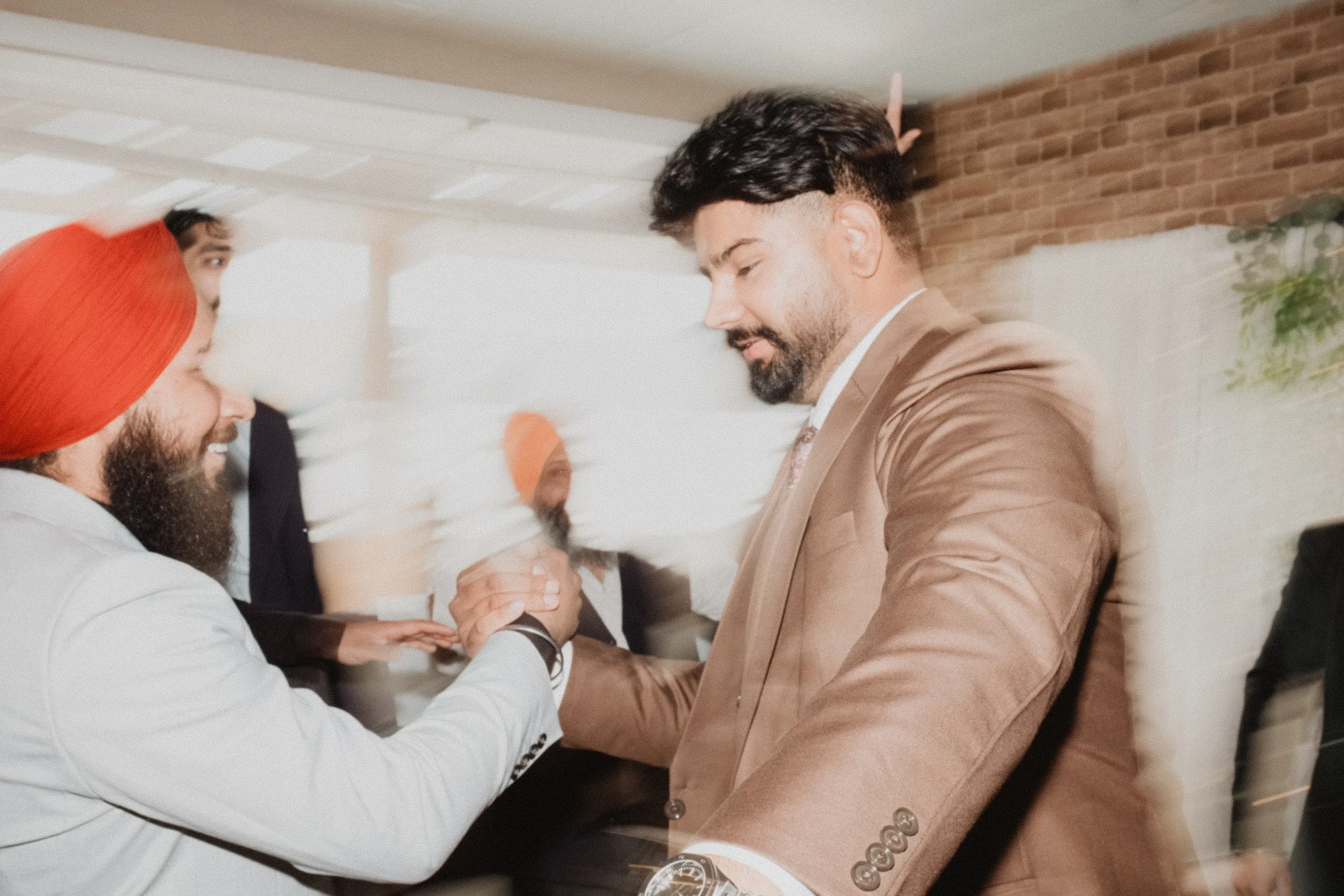 Motion blur of Kamal clasping hands with a guest in a red turban at the reception, by AD Photography