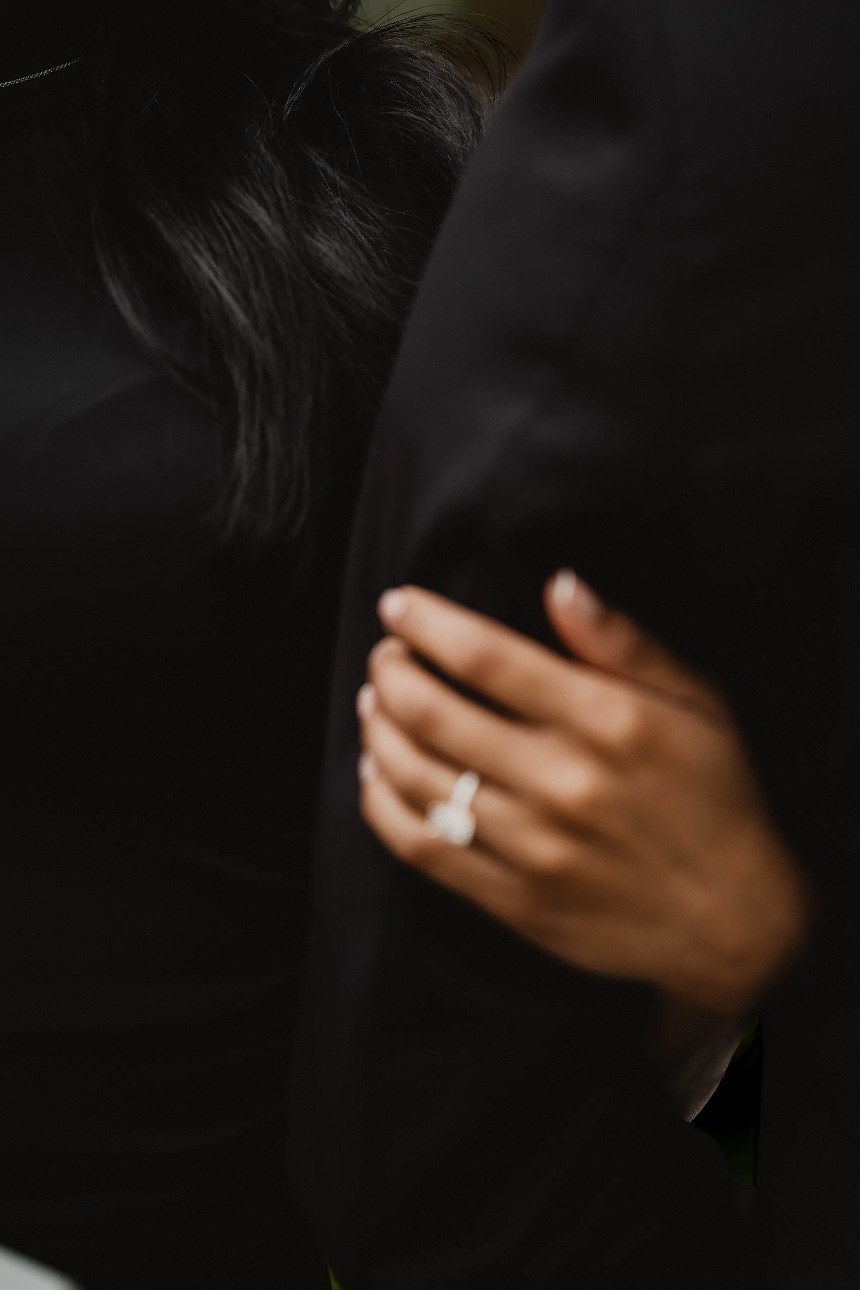 A dark, close detail of Lavina's ring hand resting on the sleeve of Raeed's black suit, by AD Photography