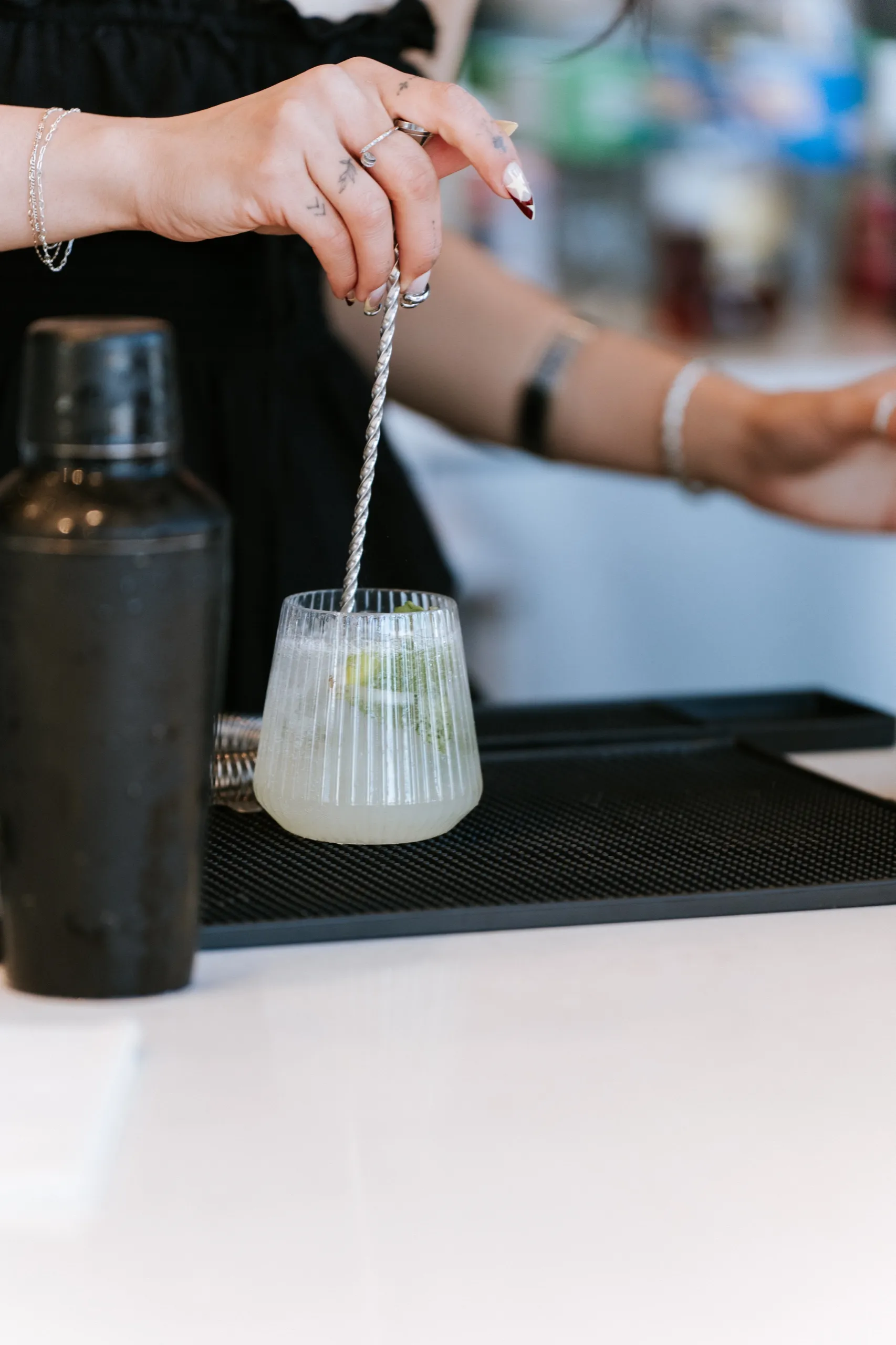 The bartender stirs a lime cocktail in a fluted glass on the bar mat, by AD Photography