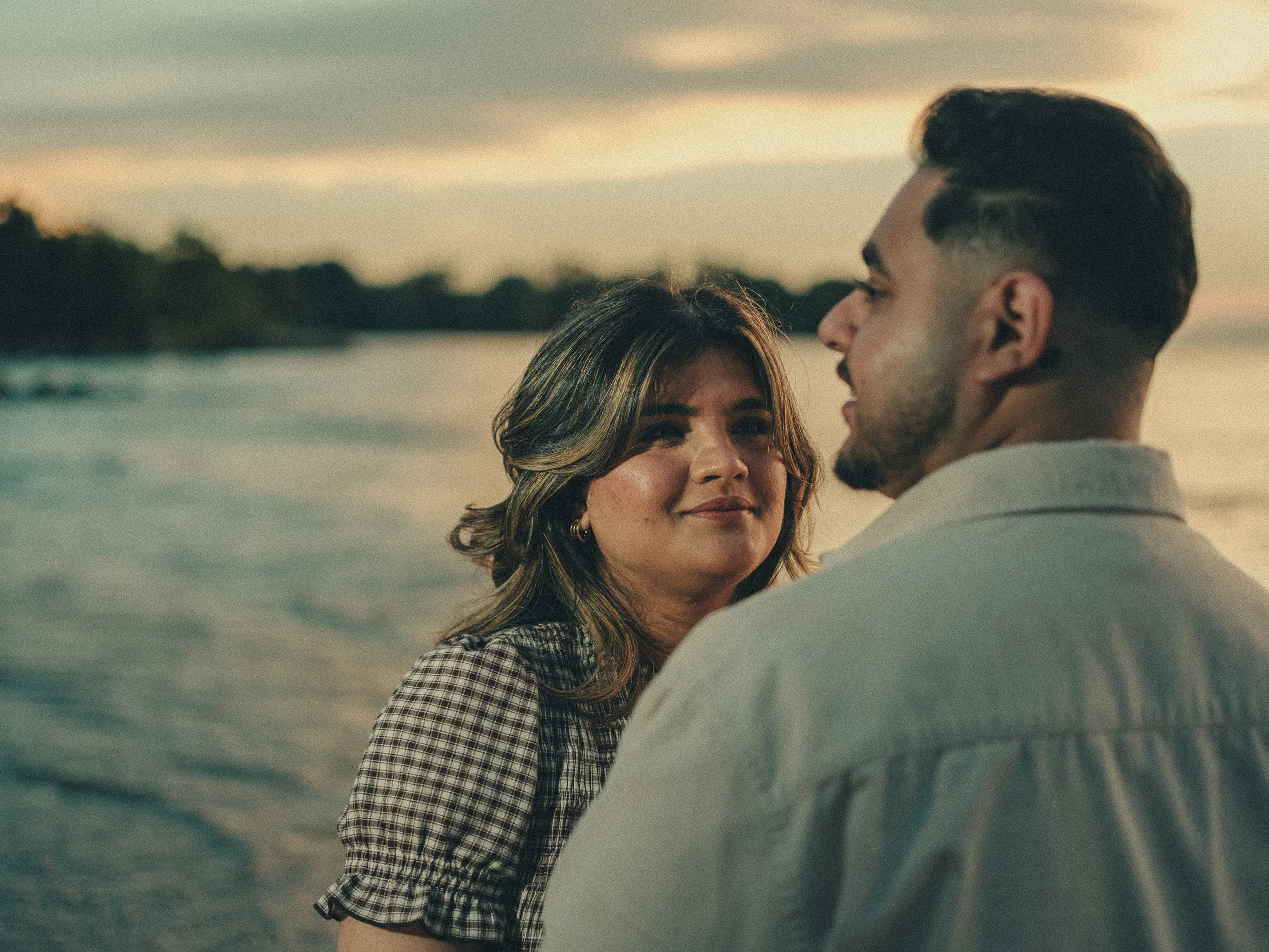 Parneet looks up at Maninder, the treed Lake Ontario shoreline dark against a warm sky, by AD Photography