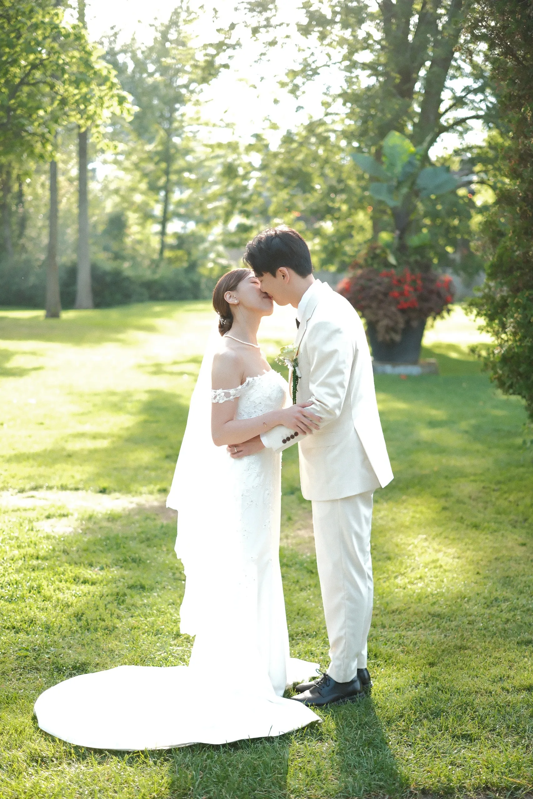 Josie and Nelson kissing on the sunlit lawn, her train fanned across the grass in Scarborough, by AD Photography