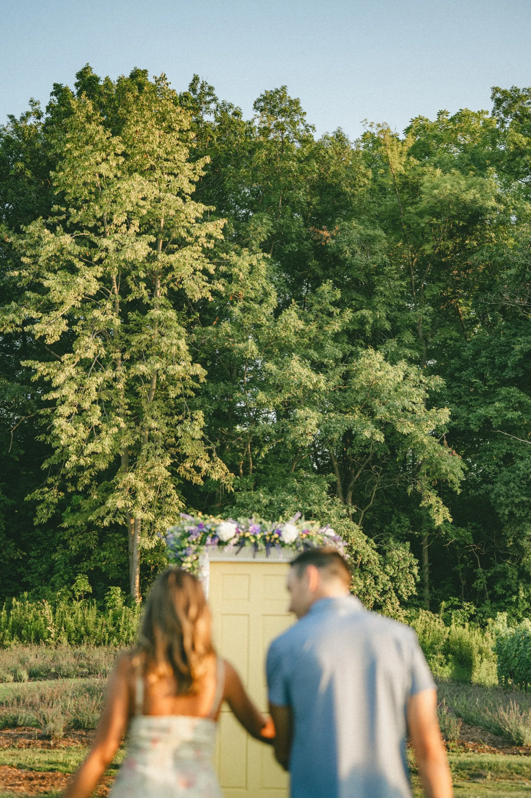 The flower framed door standing in the lavender rows, the couple soft in the foreground, by AD Photography
