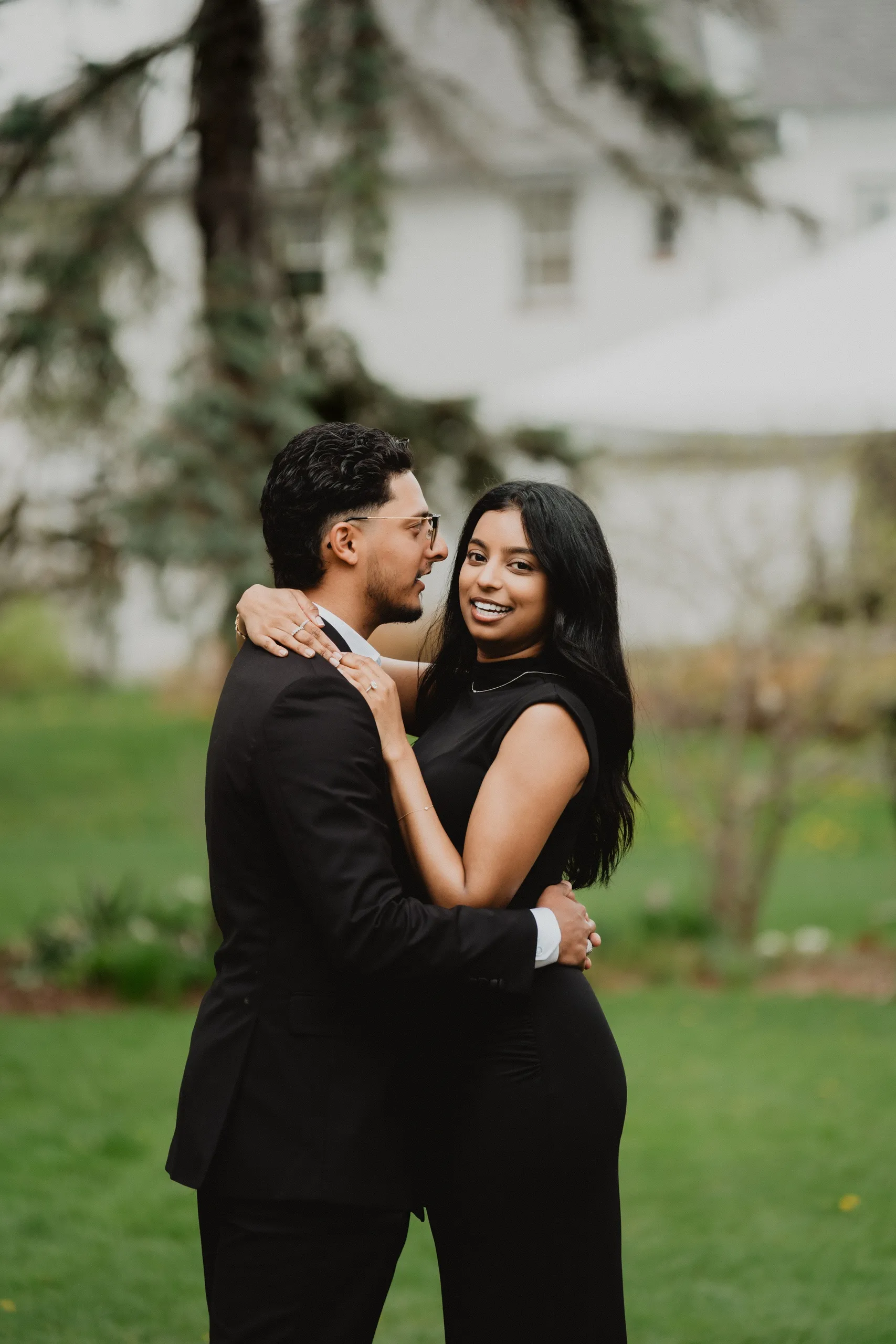 Lavina looking back over Raeed's shoulder mid embrace on the lawn in Scarborough, by AD Photography