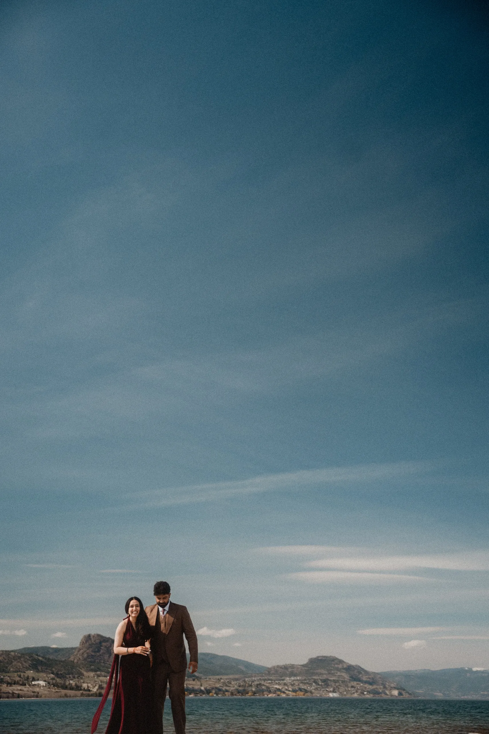 Mehak in a burgundy gown beside Kamal, dwarfed by an enormous Okanagan sky, by AD Photography