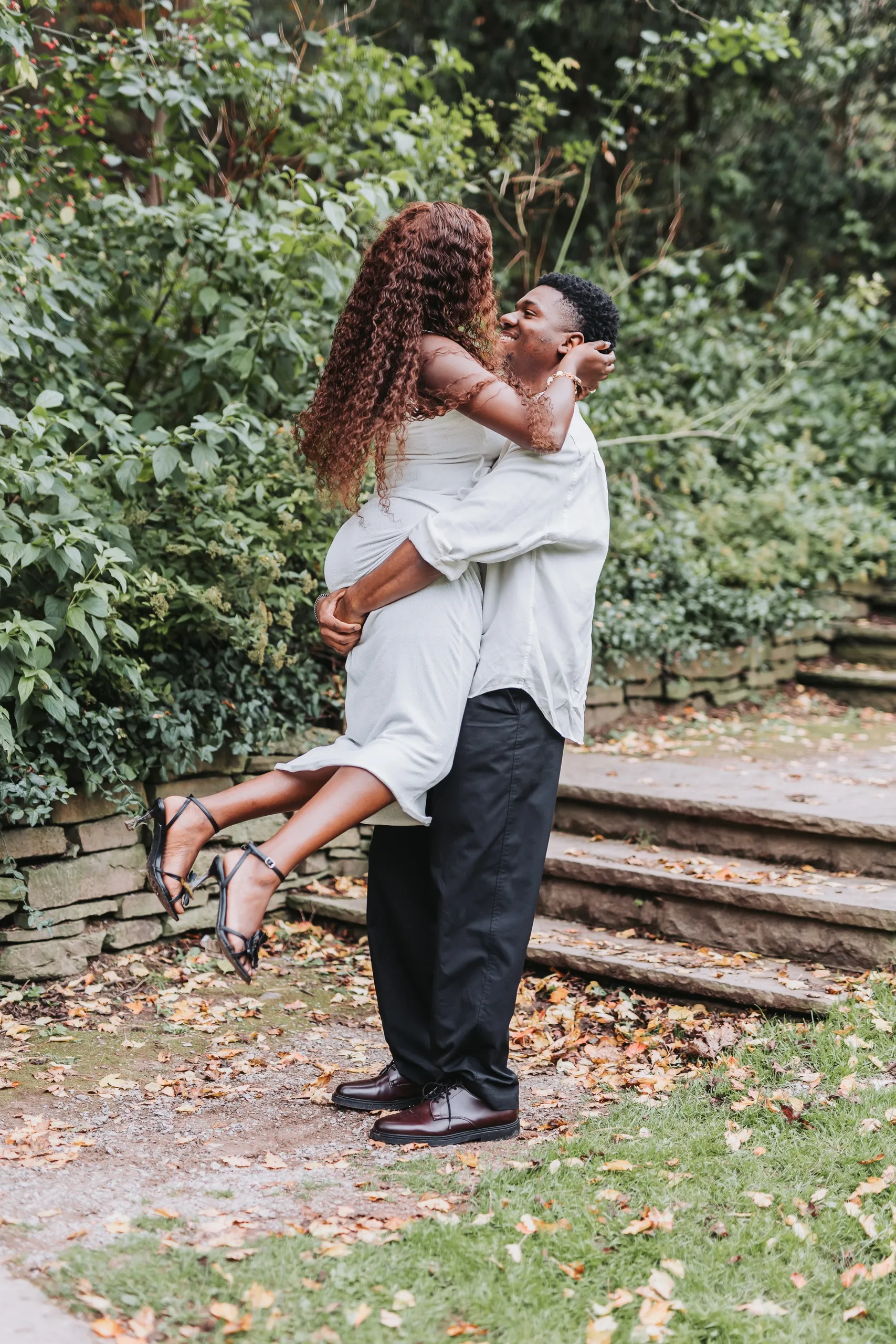Richie lifting Aimee off her feet beside the old stone steps, her heels kicked back, by AD Photography