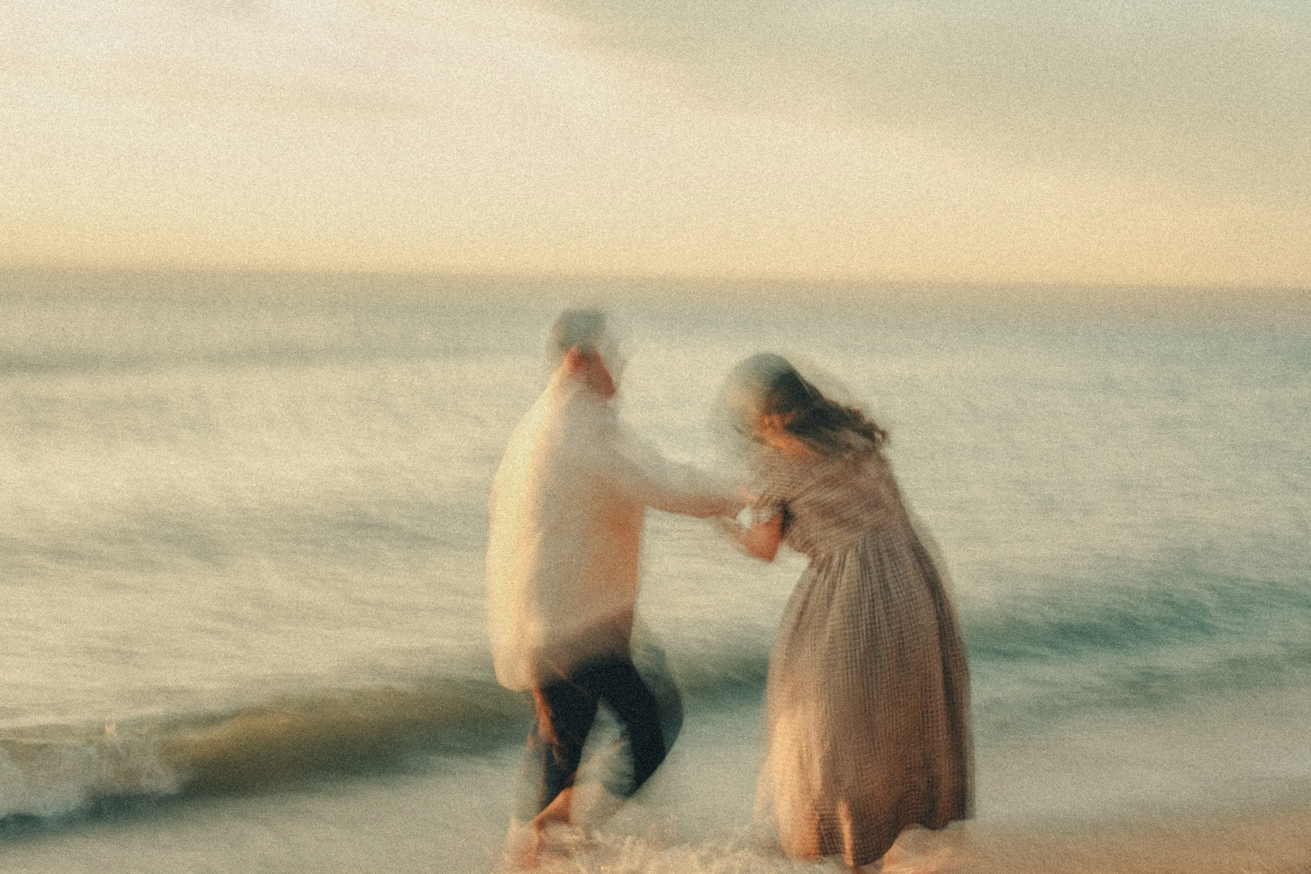 Ghosted by a slow shutter, Maninder and Parneet spin in the pale surf, hands still joined, by AD Photography