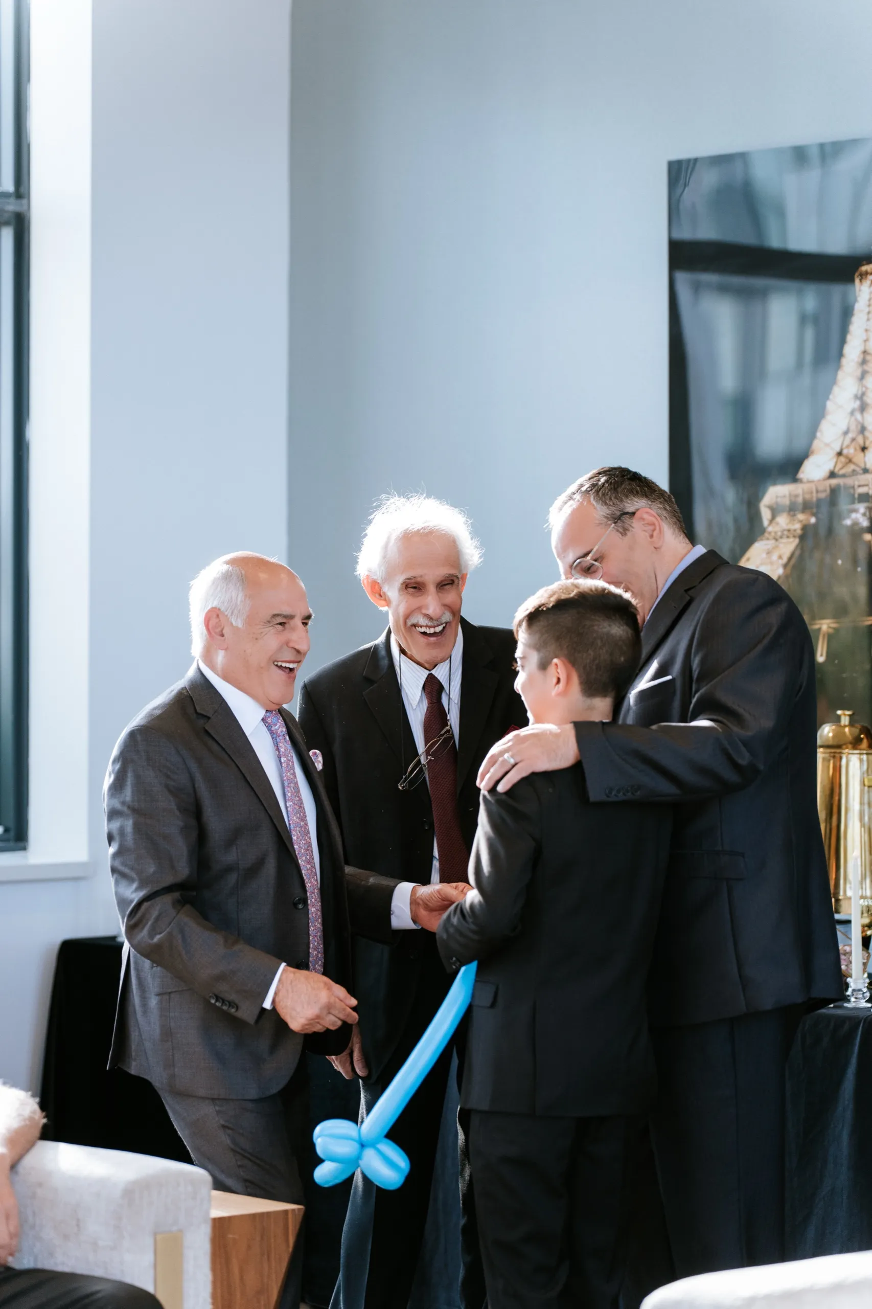 Three men in suits laugh with a boy holding a blue balloon sword, by AD Photography