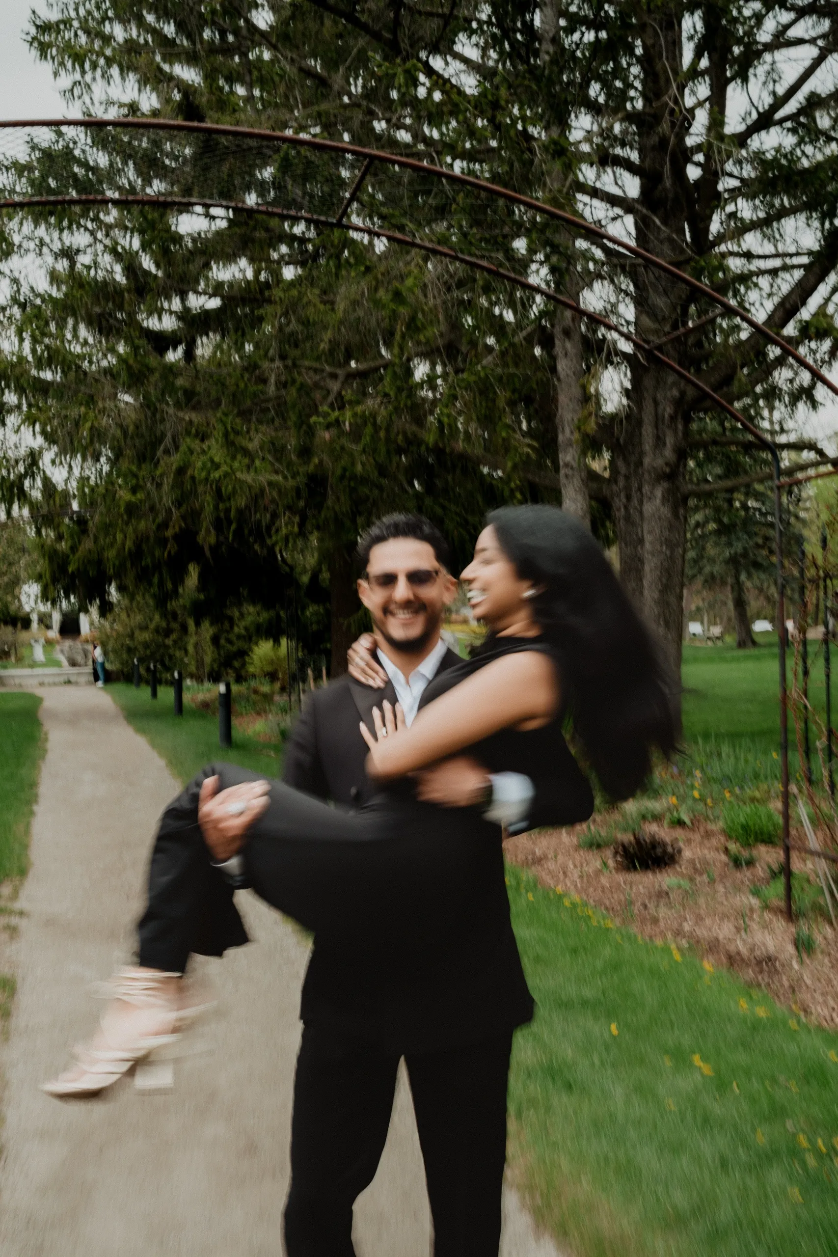 A motion blurred frame of Raeed lifting Lavina off her feet on the garden path, by AD Photography