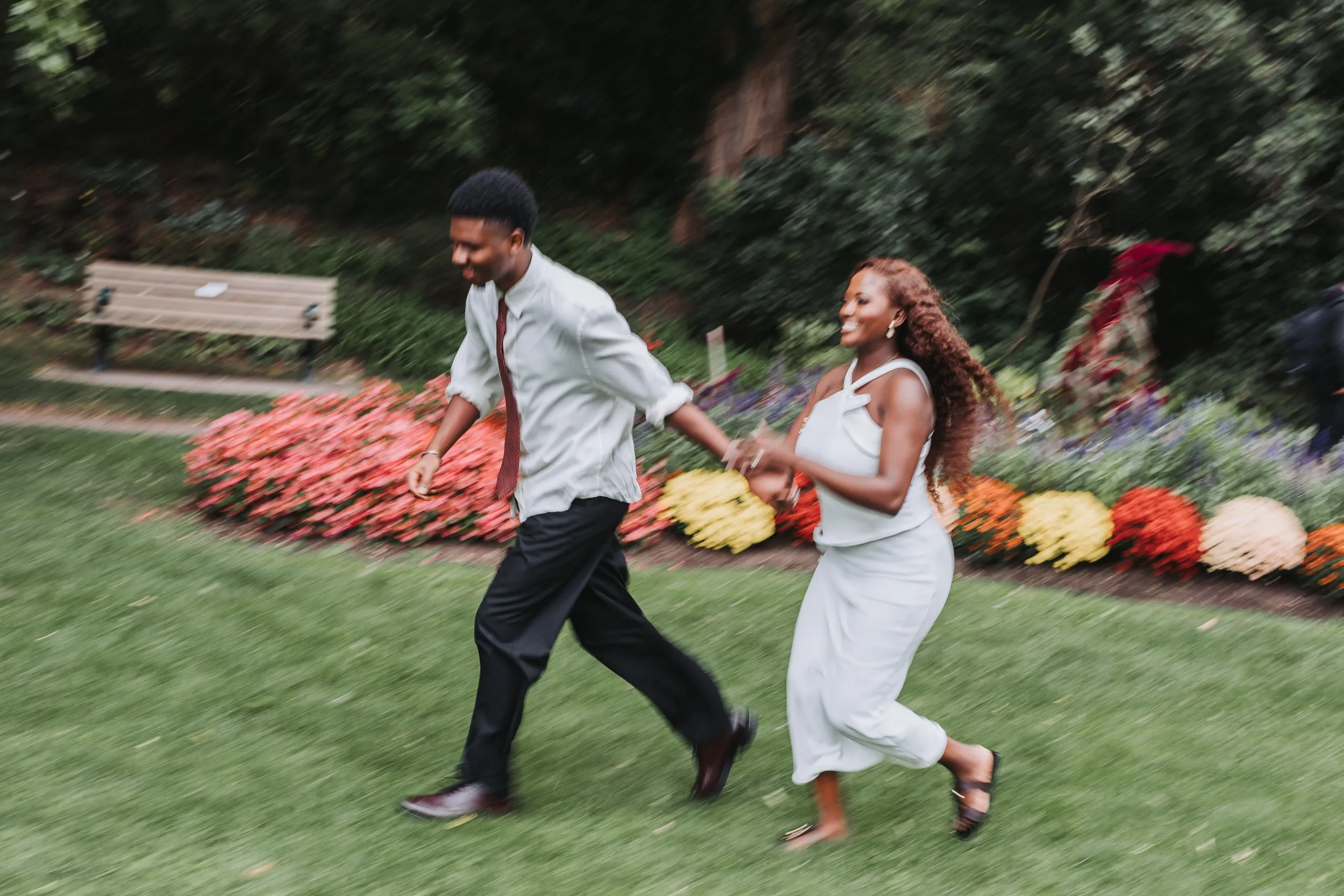 A panned motion blur of Richie and Aimee running past beds of red and yellow mums, by AD Photography