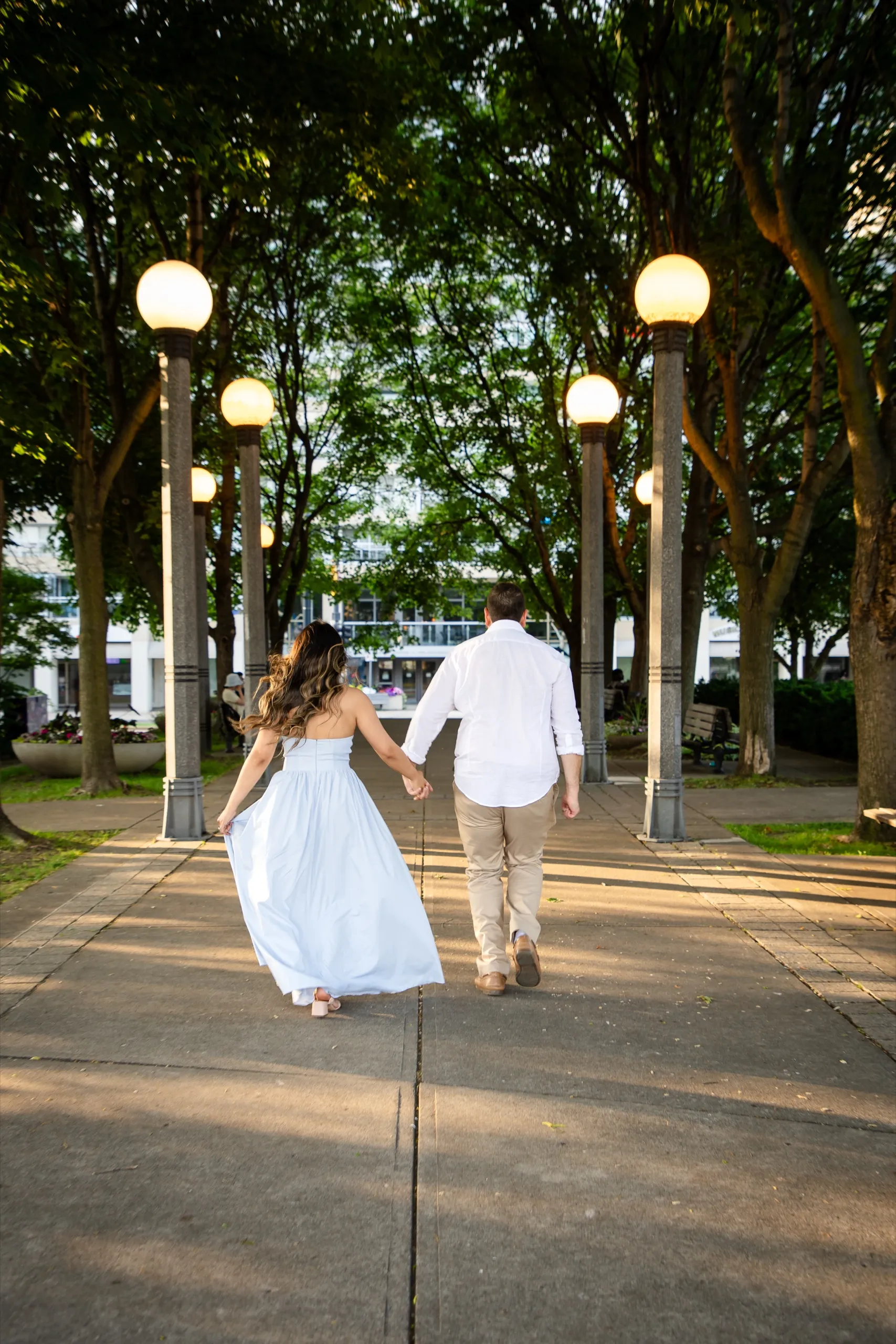 Margarita and Mike walking away down the lamp lined promenade at the Toronto Harbourfront at sunset, by AD Photography