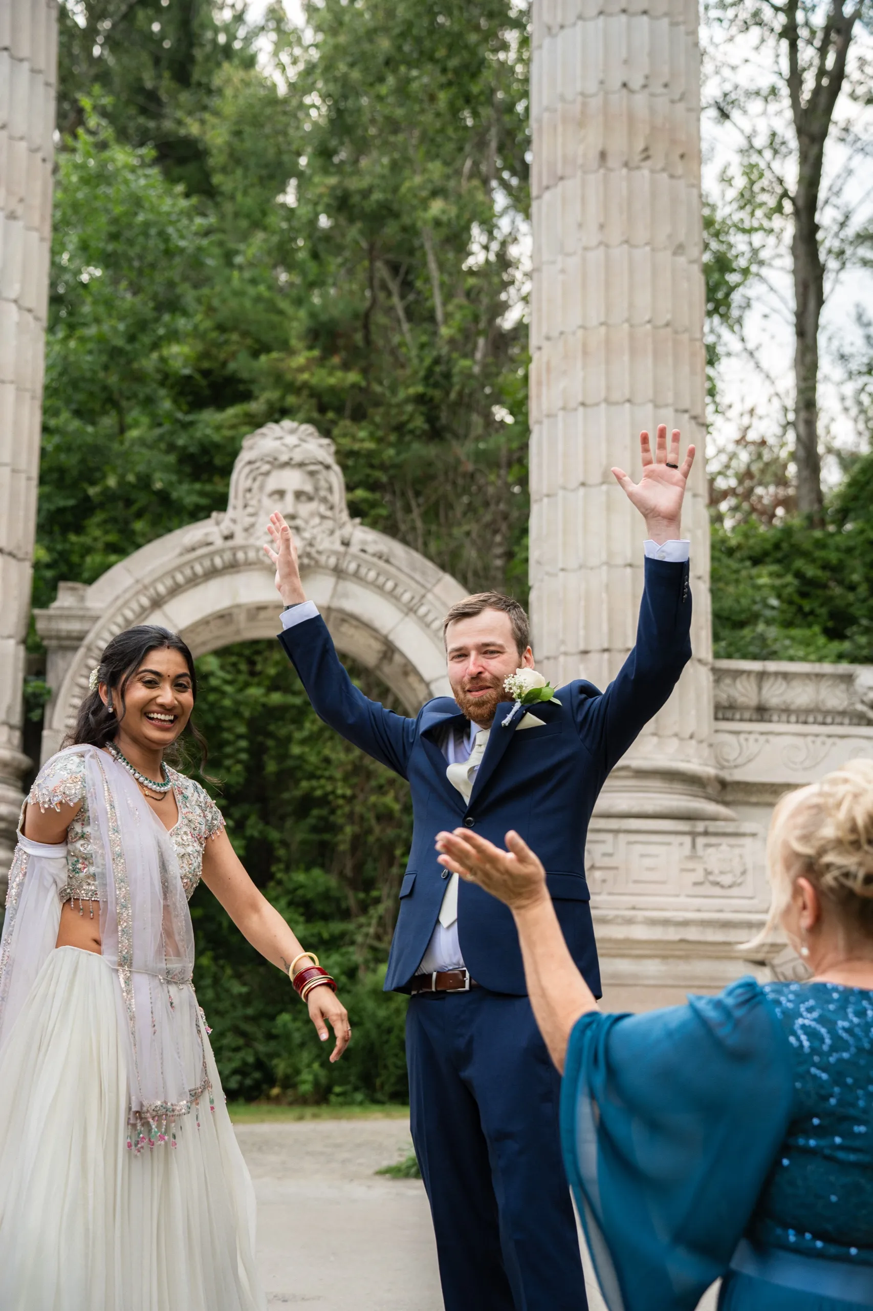 Derek throws his hands up celebrating as Nidhi laughs beside him, newly married., by AD Photography