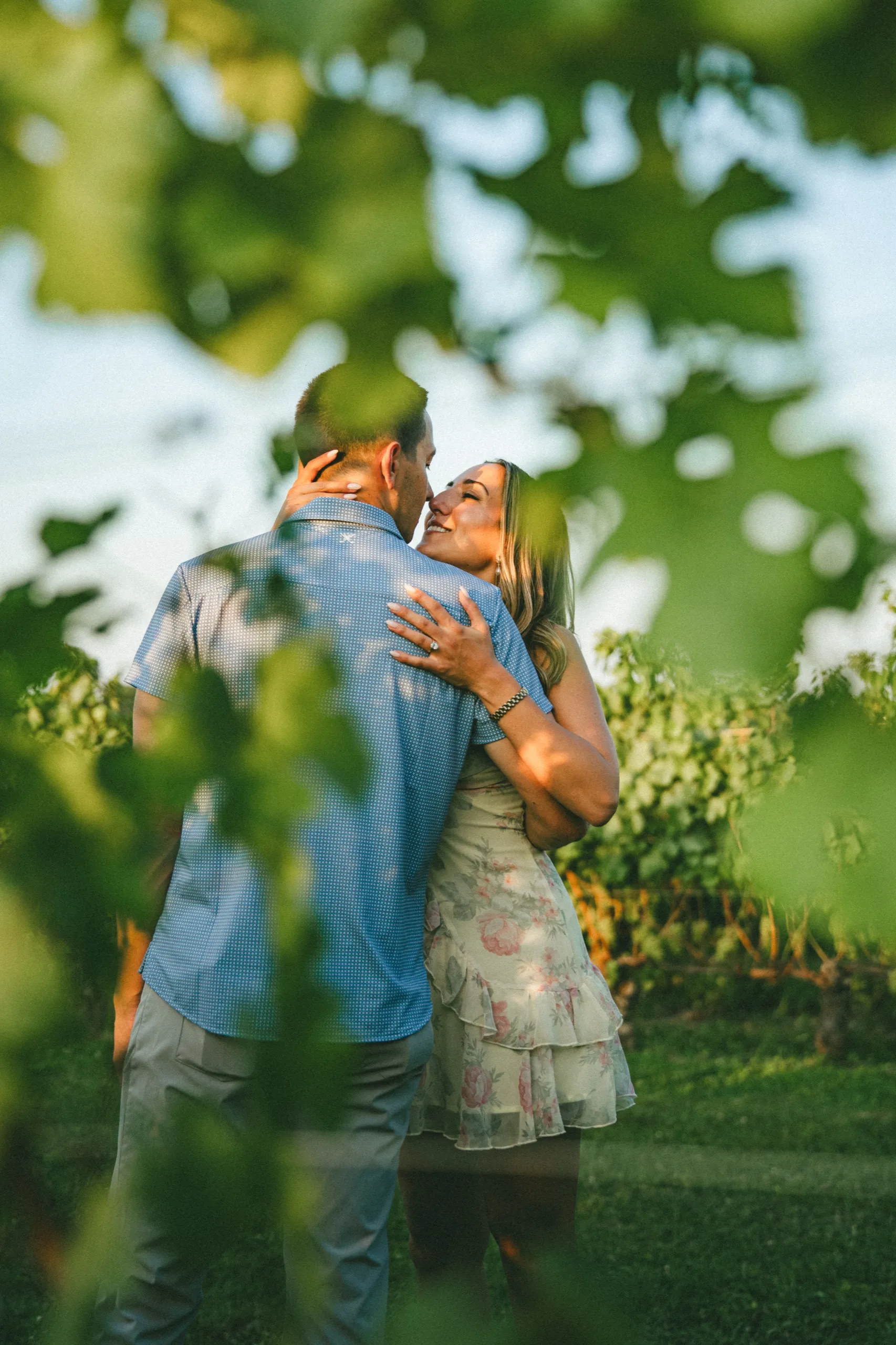 Ashley and Donald framed through vine leaves, her hand behind his neck, by AD Photography