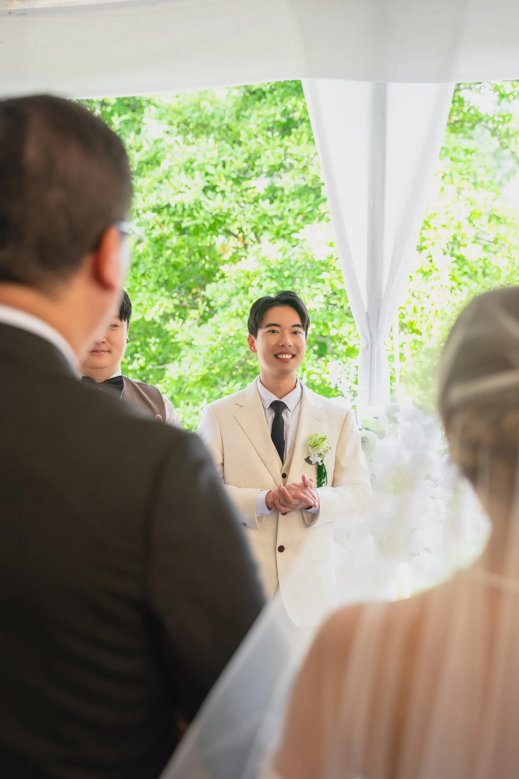 Nelson waiting at the altar, seen between the shoulders of seated wedding guests, by AD Photography