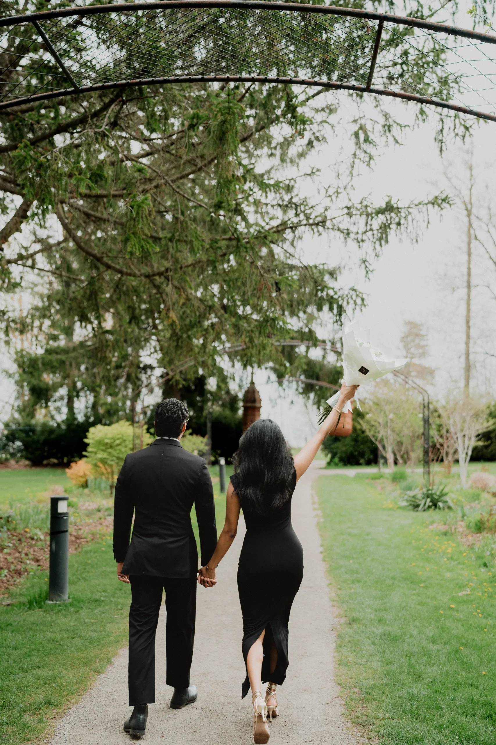 Lavina raising her bouquet overhead as she and Raeed walk away at Guild Park and Gardens, by AD Photography