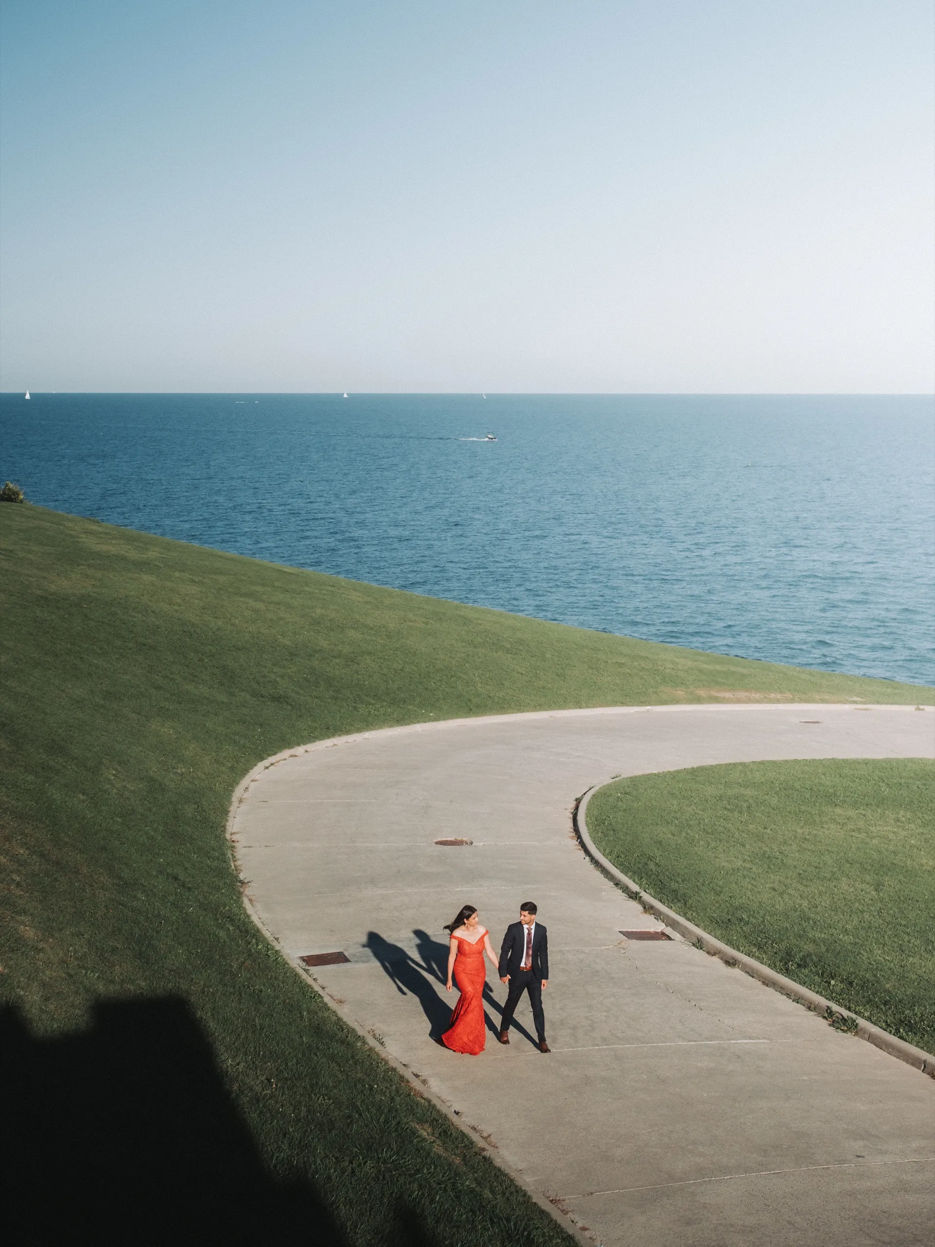 The couple walks a curving lakeside path in a minimalist frame of grass and water, by AD Photography