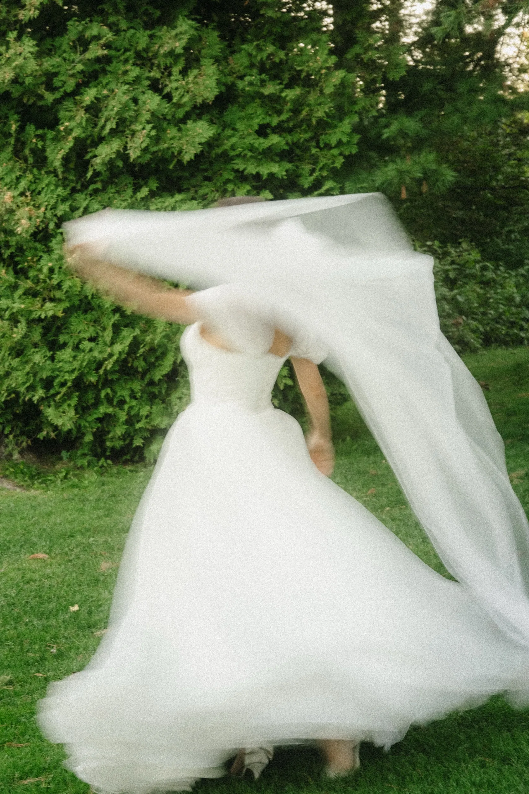Veil thrown over the bride's head mid spin, the ball gown swirling on the grass, by AD Photography