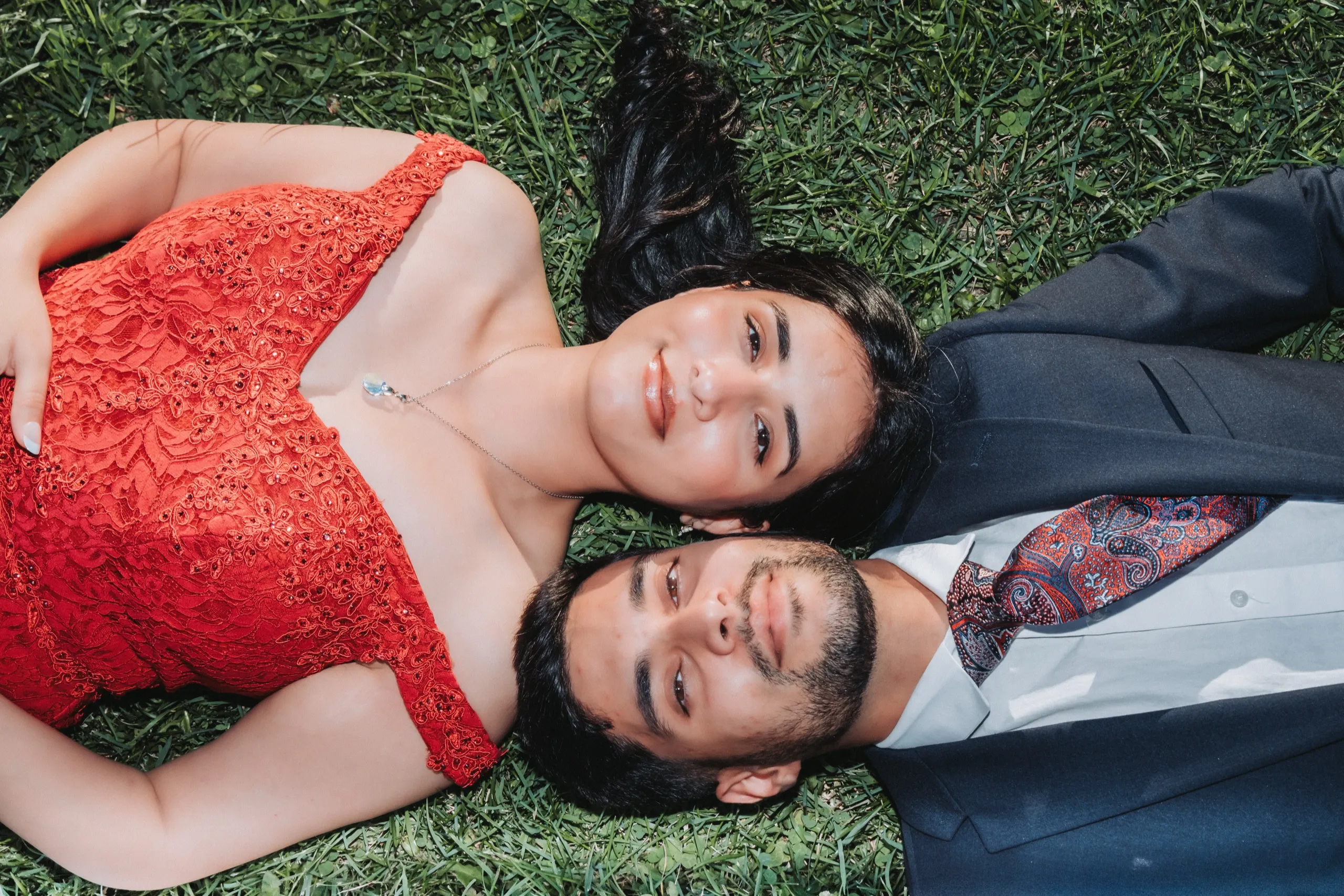 Overhead frame of the couple lying head to head in the grass, both grinning, by AD Photography